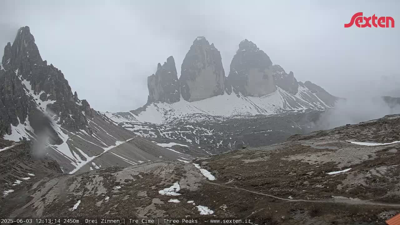 A snow-dusted, rocky mountain range is partially obscured by fog.