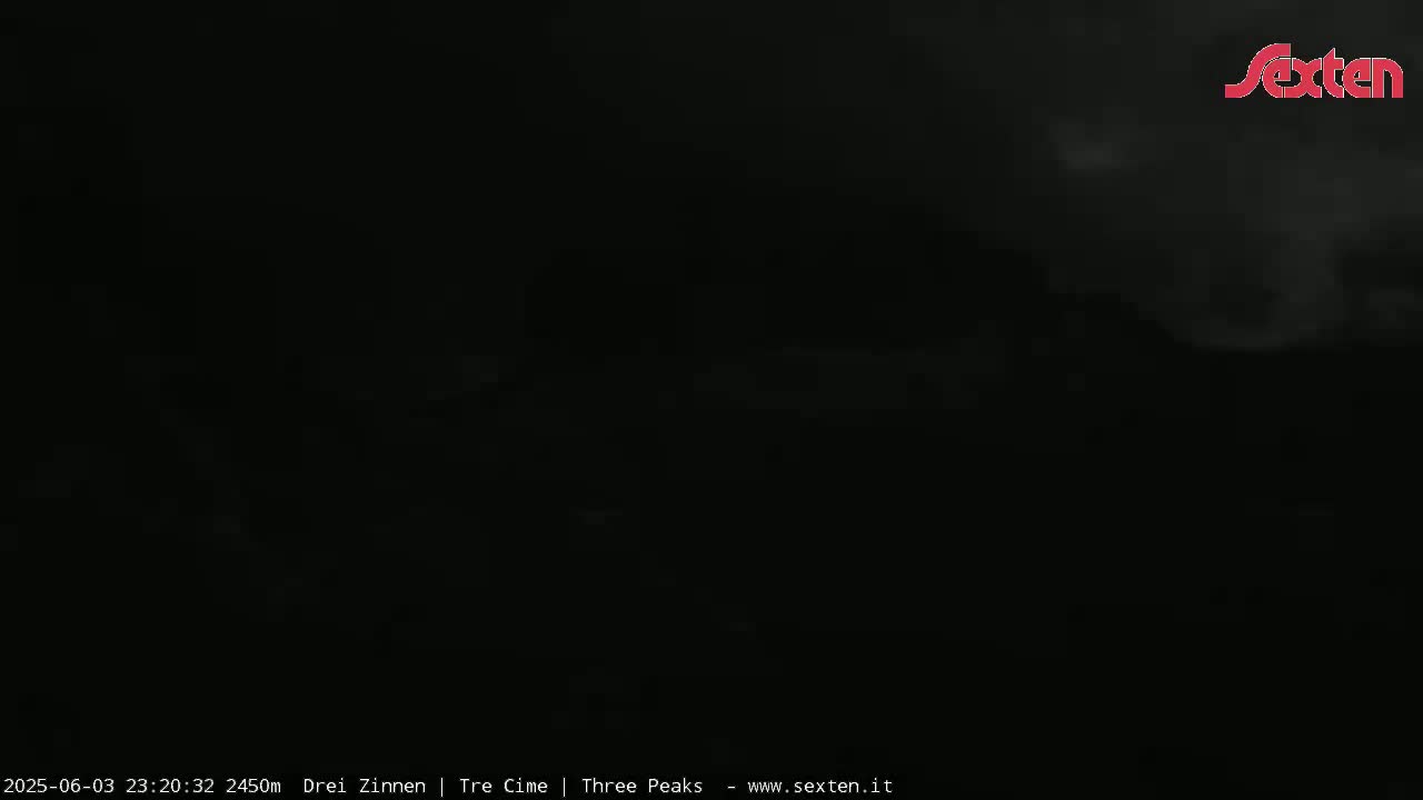 A very dark nighttime image shows a mostly obscured landscape under a cloudy sky.