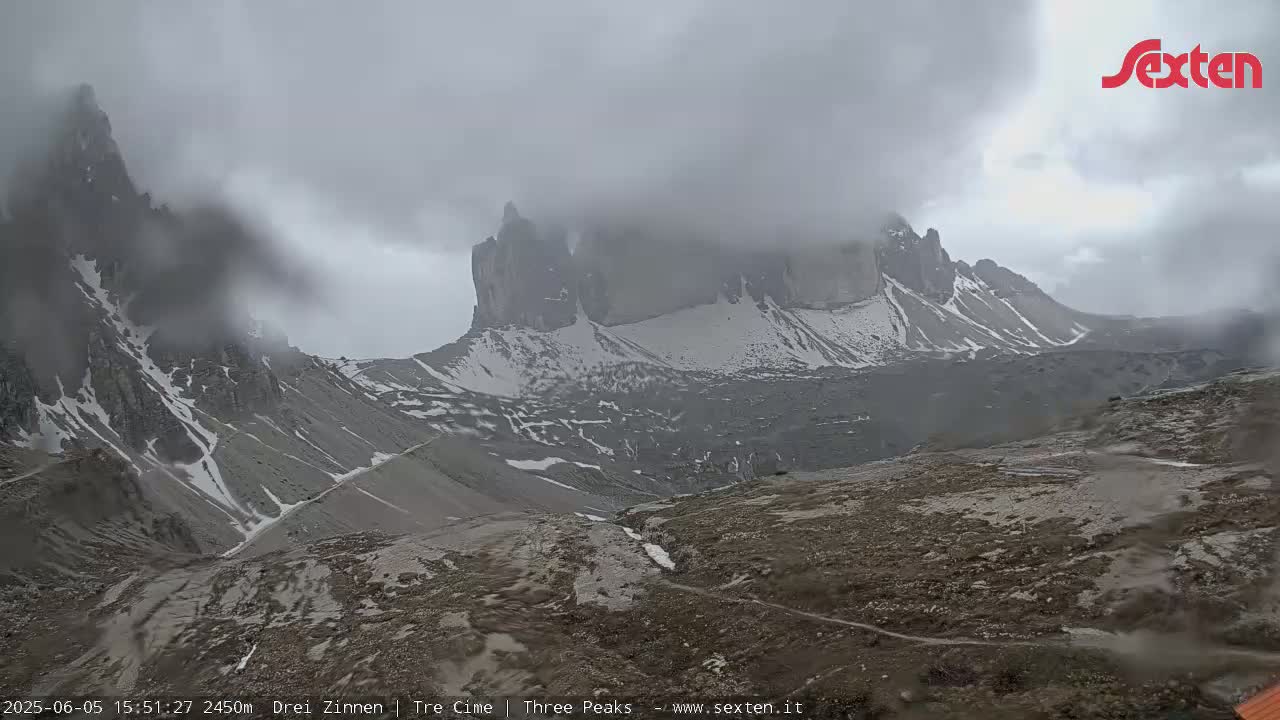 A mountain range with snow-capped peaks is partially obscured by heavy clouds and mist.