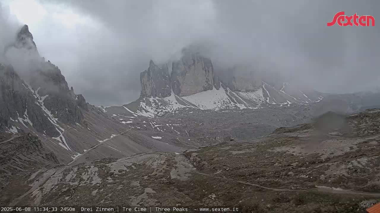 A mountain range partially obscured by fog and clouds, with some snow patches visible on the higher elevations.
