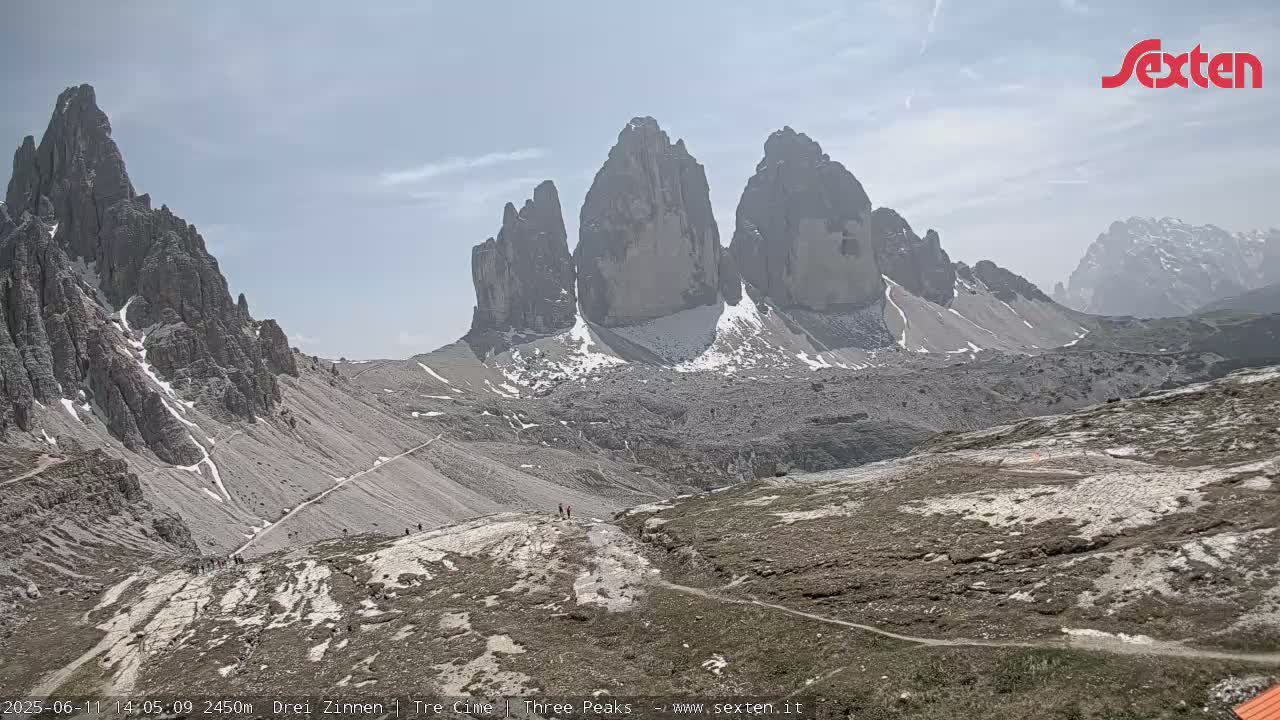 A mountain range with several prominent peaks, some with patches of snow, is visible under a mostly clear sky.