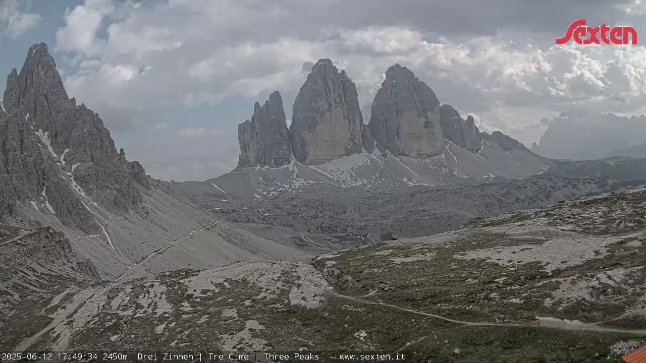 A view of rocky, mountainous terrain under a partly cloudy sky shows several tall, jagged peaks in the distance.