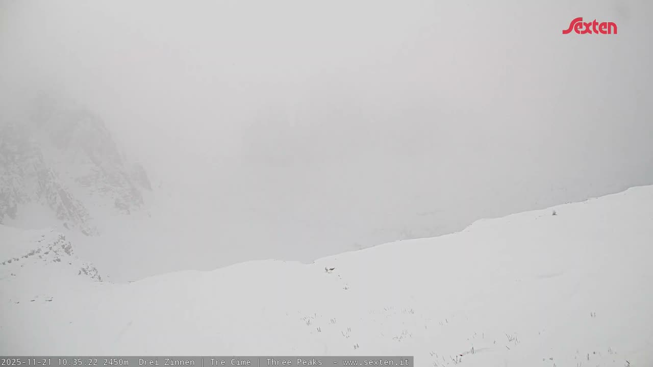 A snow-covered mountain landscape is visible under very dense fog or heavy cloud cover, creating extremely poor visibility.