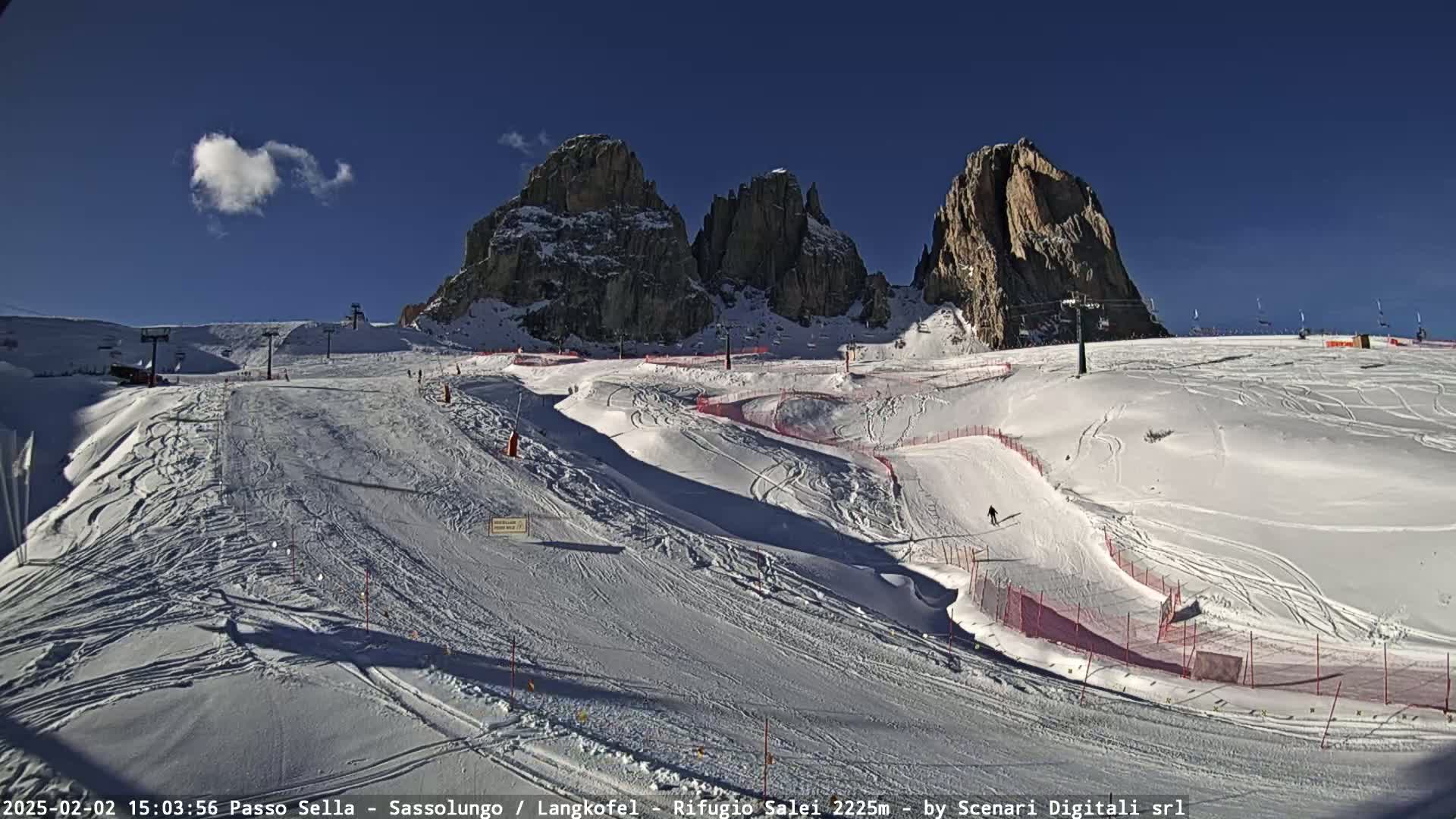 A sunny, snow-covered ski slope with ski lifts and rocky mountains in the background.