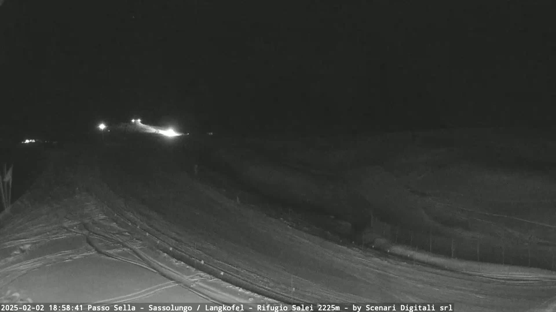 A nighttime, snowy landscape is shown with a road and faint light sources in the distance.