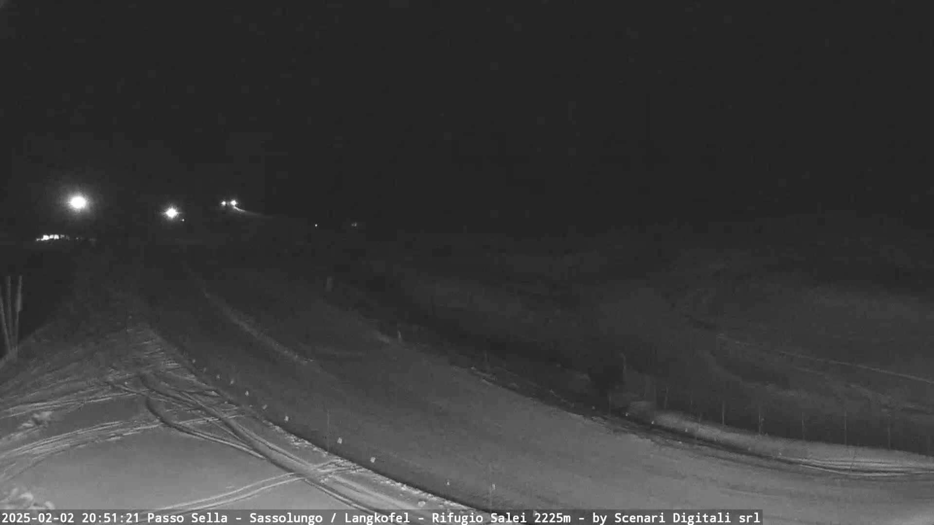 A nighttime view of a snow-covered road with a few vehicle headlights visible in the distance.
