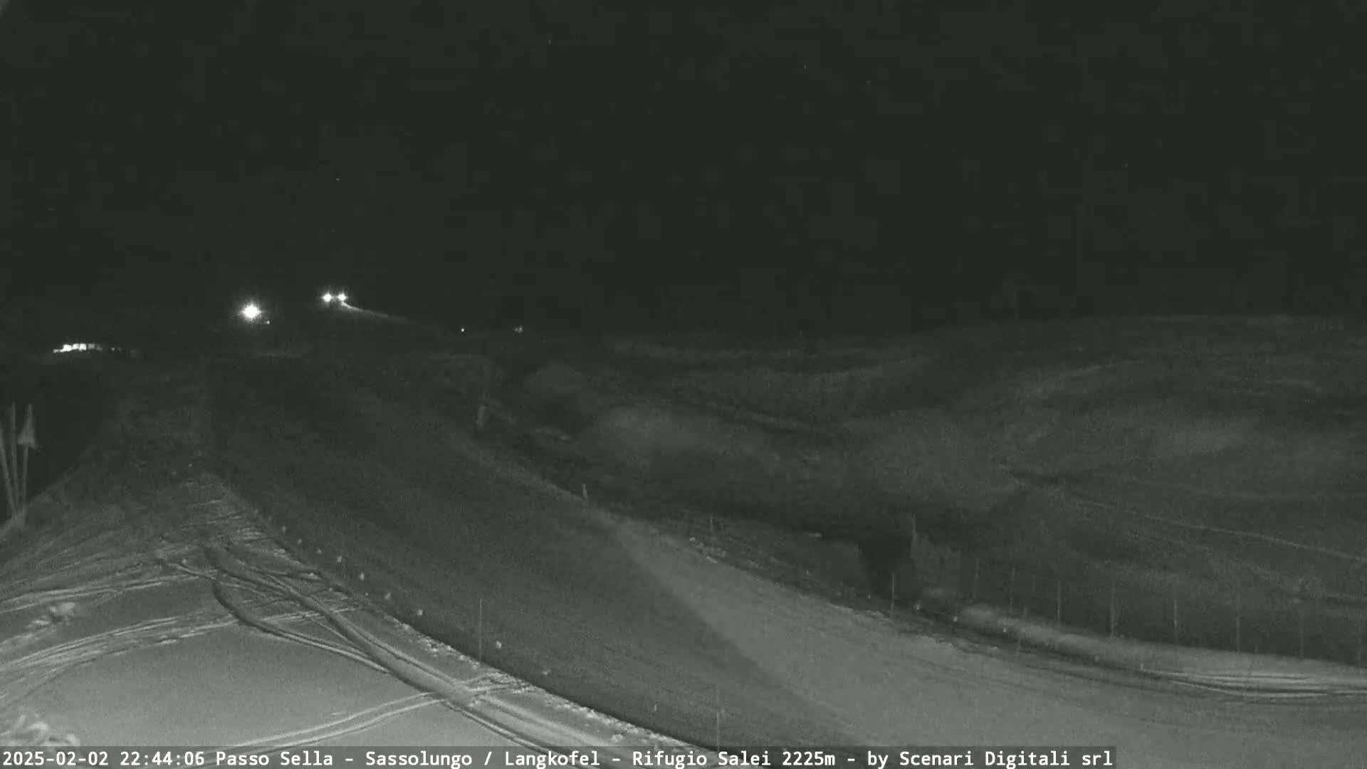 A nighttime, snow-covered road with a few vehicles driving on it under a dark sky.