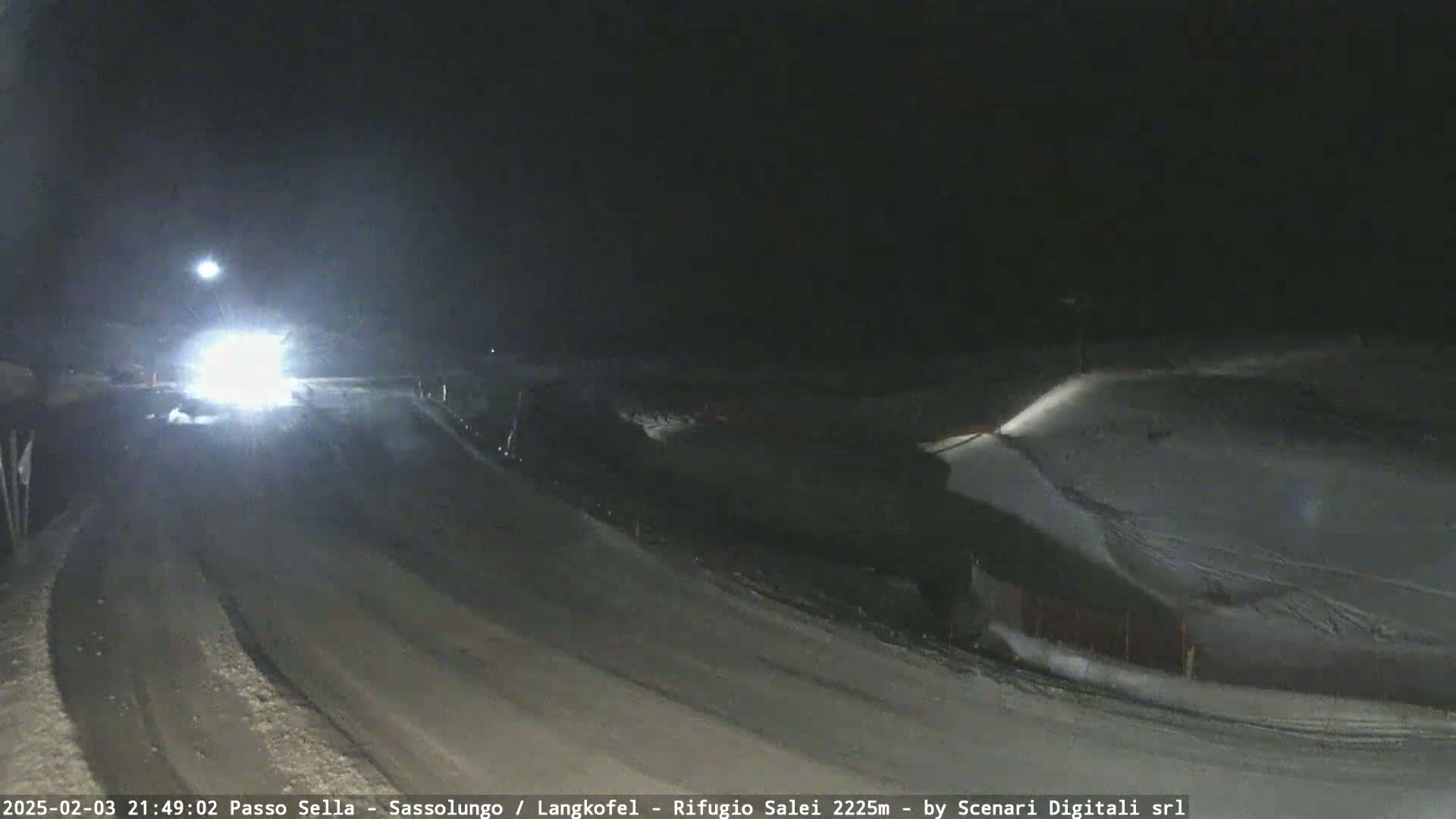 A snow-covered road curves gently at night, with a vehicle's headlights illuminating the area ahead.
