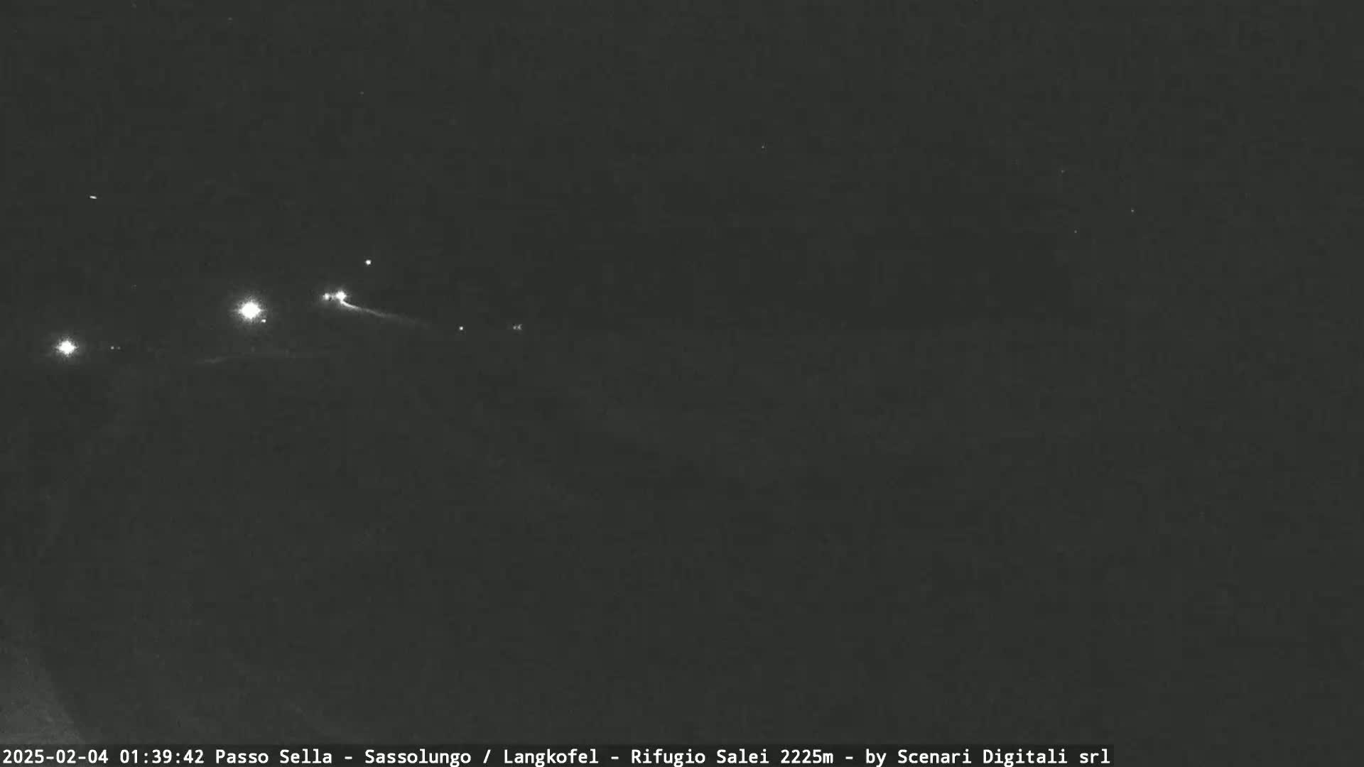 A nighttime long shot shows several distant lights on a dark, possibly mountainous landscape under a clear sky.