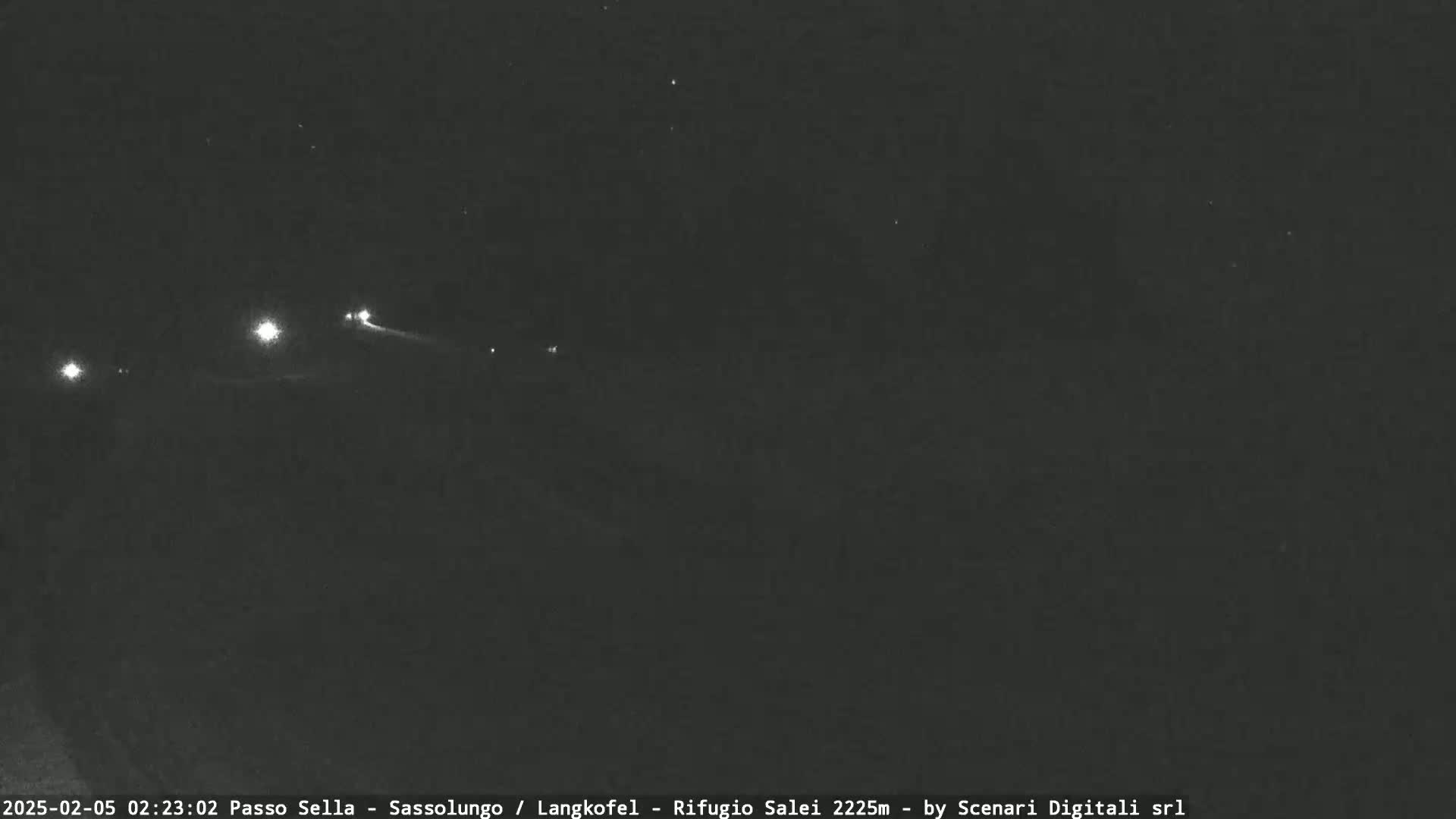 A nighttime long shot shows several distant lights, possibly headlights, on a dark road or landscape.