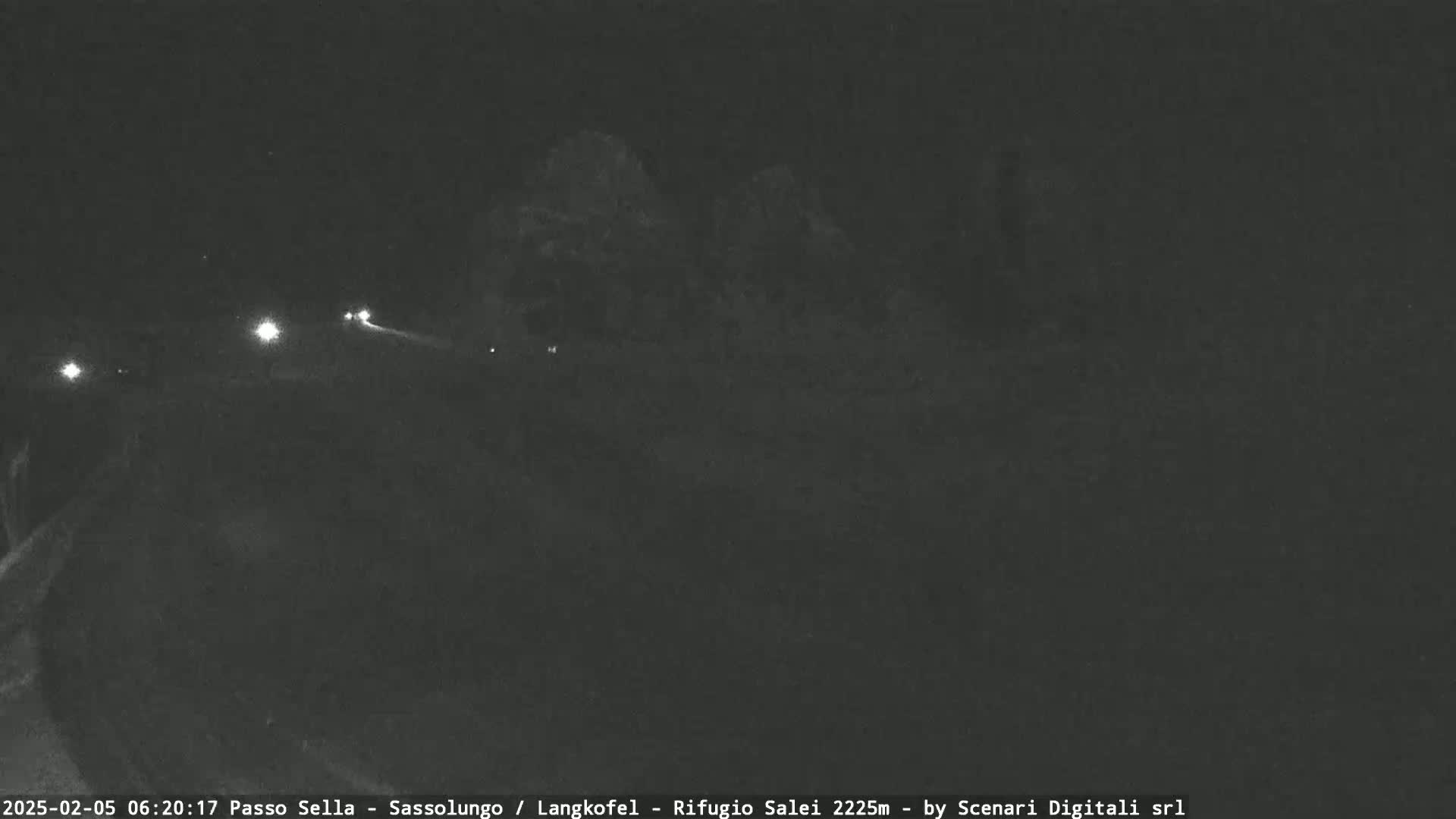 A nighttime, low-light view of a dark, mountainous landscape with a few distant headlights visible.