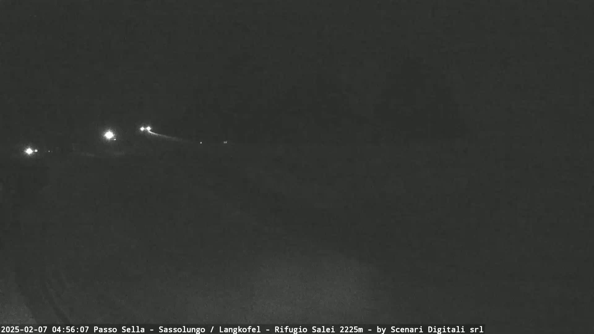 At night, a dark road shows a few vehicle headlights in the distance.