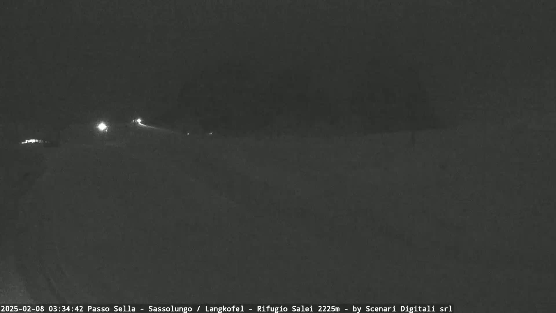A dark, nighttime scene shows a road with a few distant vehicle headlights visible under a clear sky.