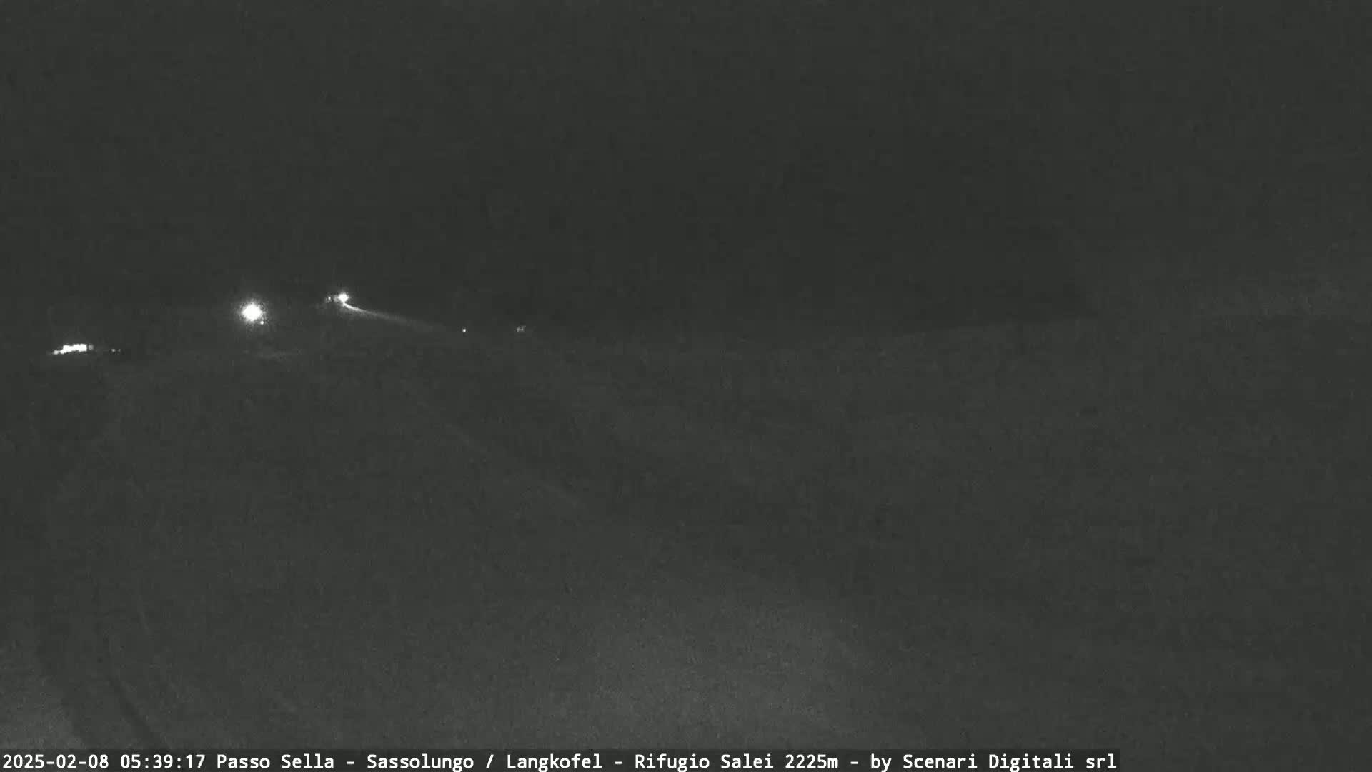 A dark, nighttime scene shows a road with a few distant headlights visible under a clear sky.