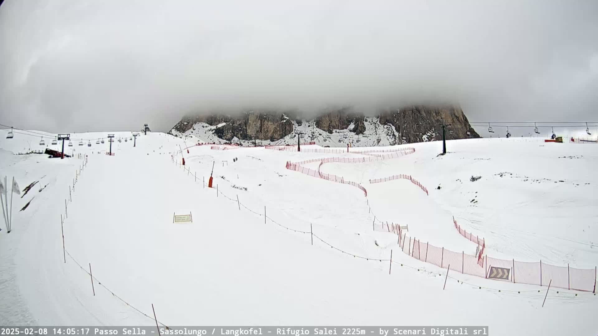 A snow-covered ski slope with chairlifts and red safety nets is visible beneath a foggy sky.
