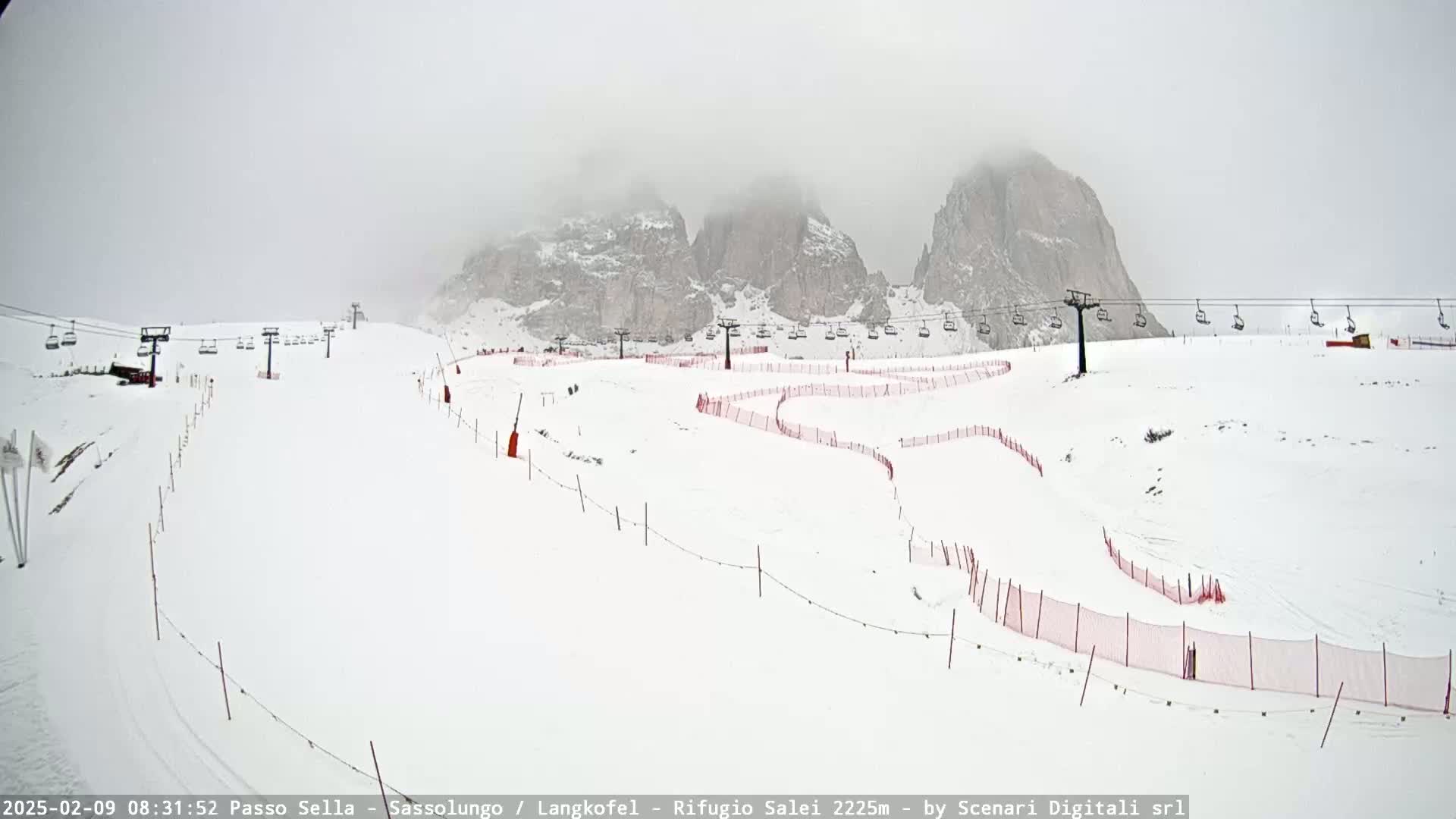 A snowy ski slope with chairlifts and red safety netting is visible, with foggy mountains in the background.
