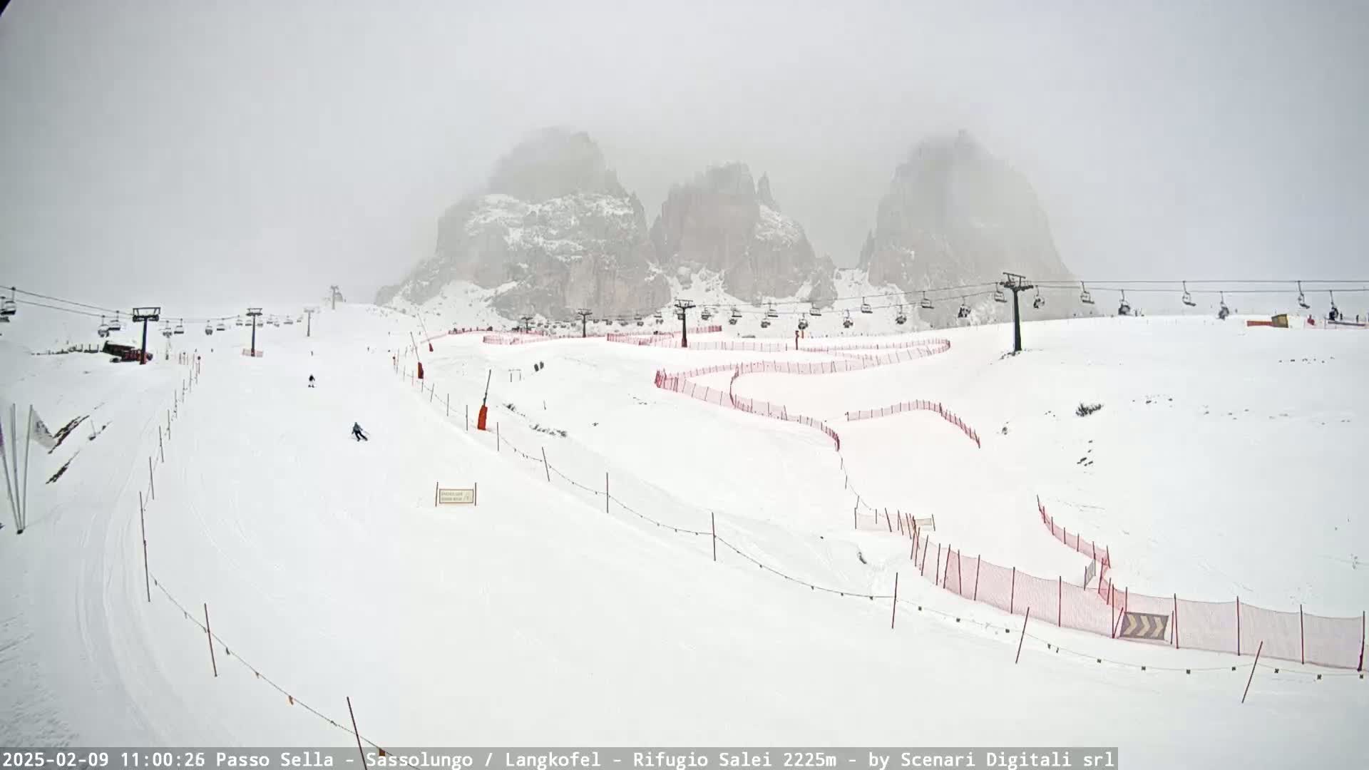 A snowy ski slope with chairlifts and red safety nets is visible against a backdrop of fog-covered mountains.