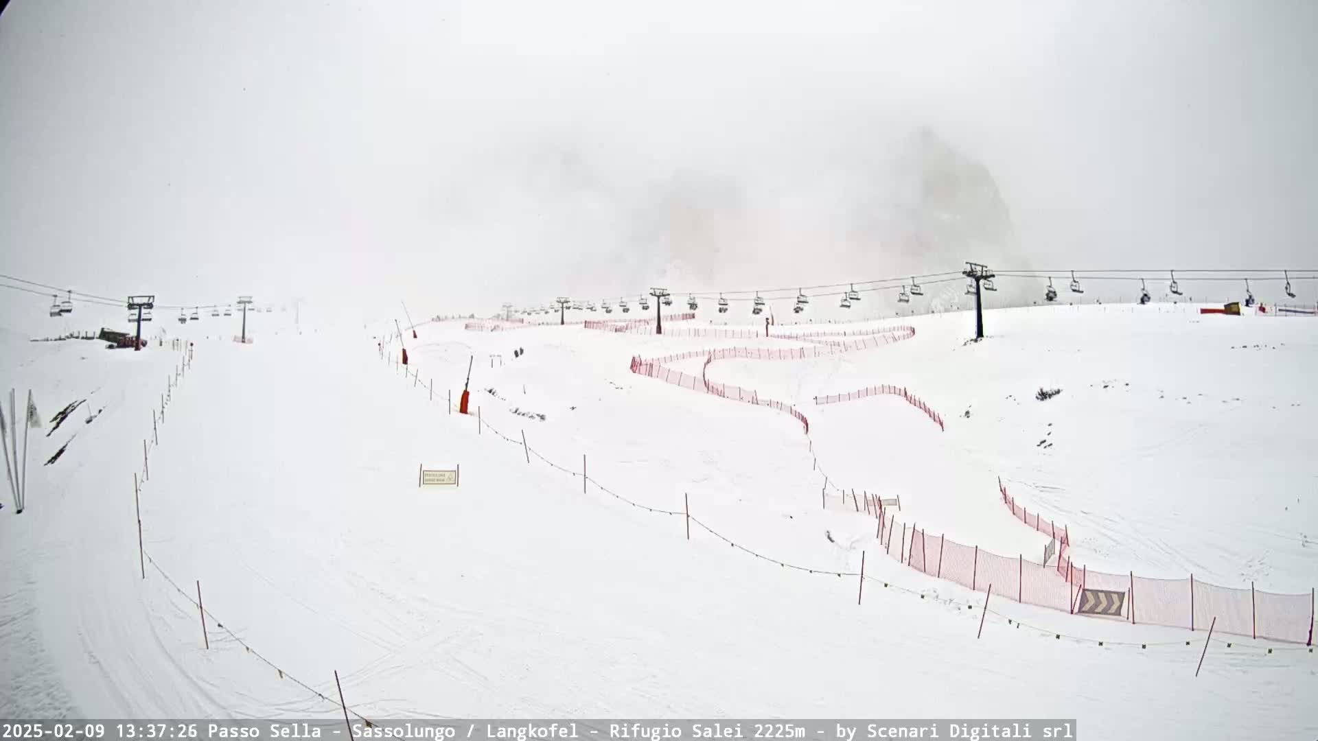 A snowy ski slope with chairlifts and red safety netting is visible under overcast skies.