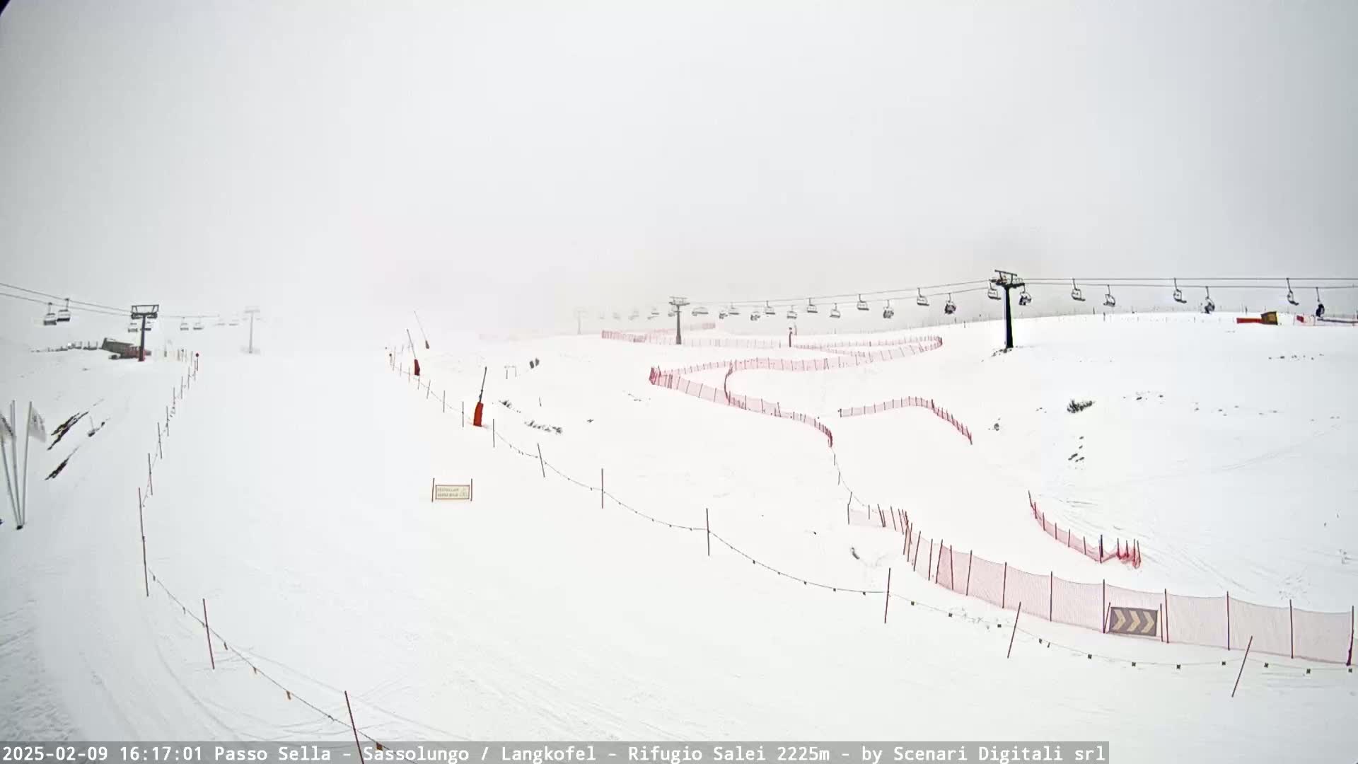 A snow-covered ski slope with chairlifts and red safety netting is visible in foggy conditions.