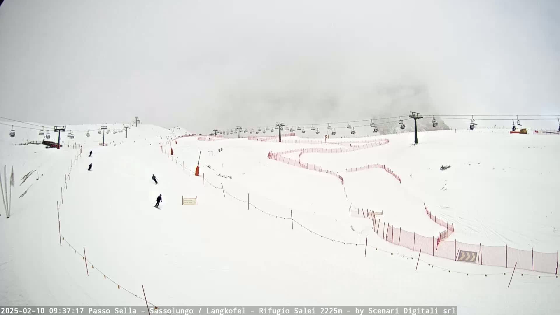 A snowy ski slope with several chairlifts and a few skiers visible under an overcast sky.