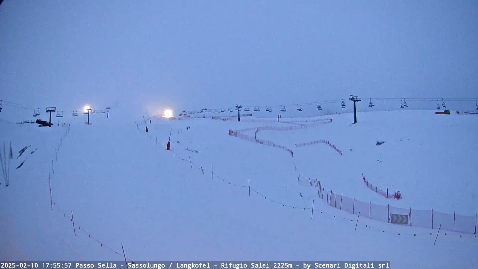 A snow-covered ski slope with chairlifts and safety nets under a dusky sky.
