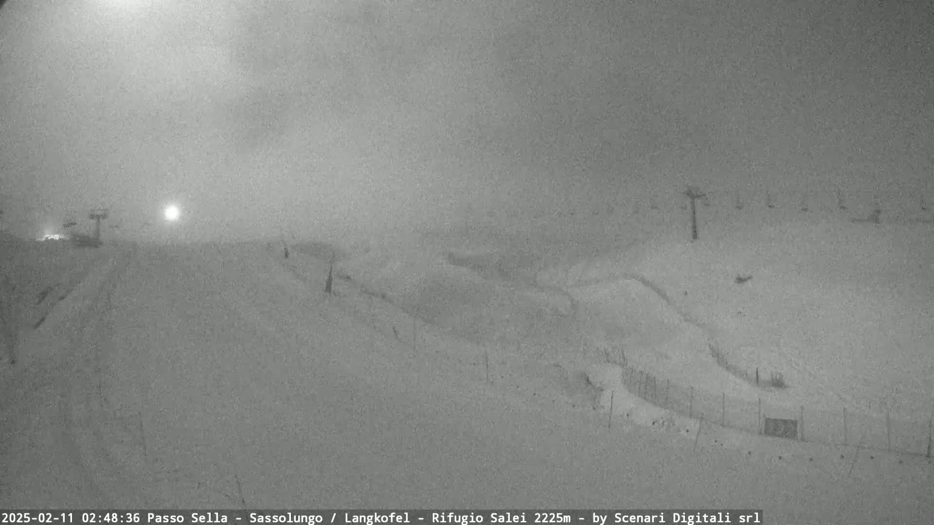 A snowy, overcast scene shows a ski slope with sparsely visible ski lifts and fences.