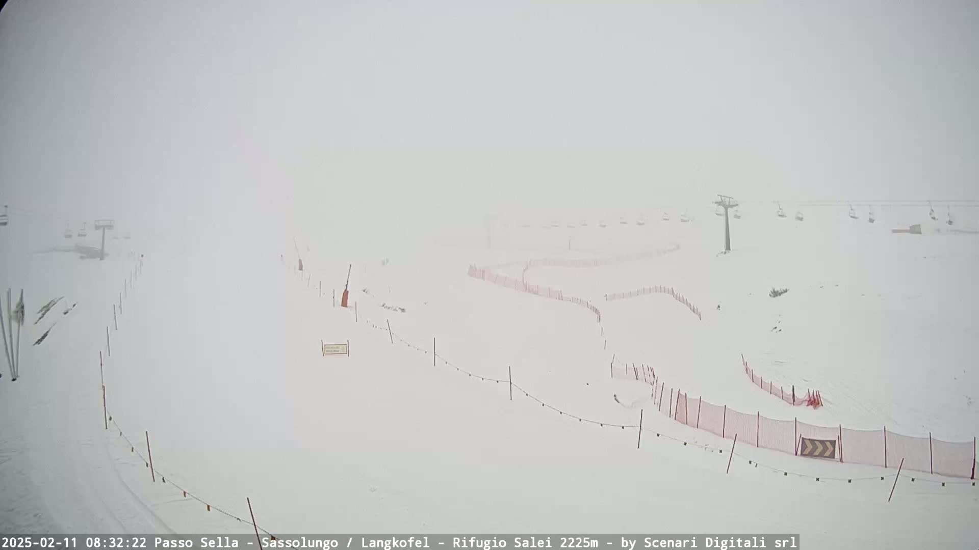 A snow-covered ski slope is shrouded in heavy fog, with ski lifts and safety fences partially visible.