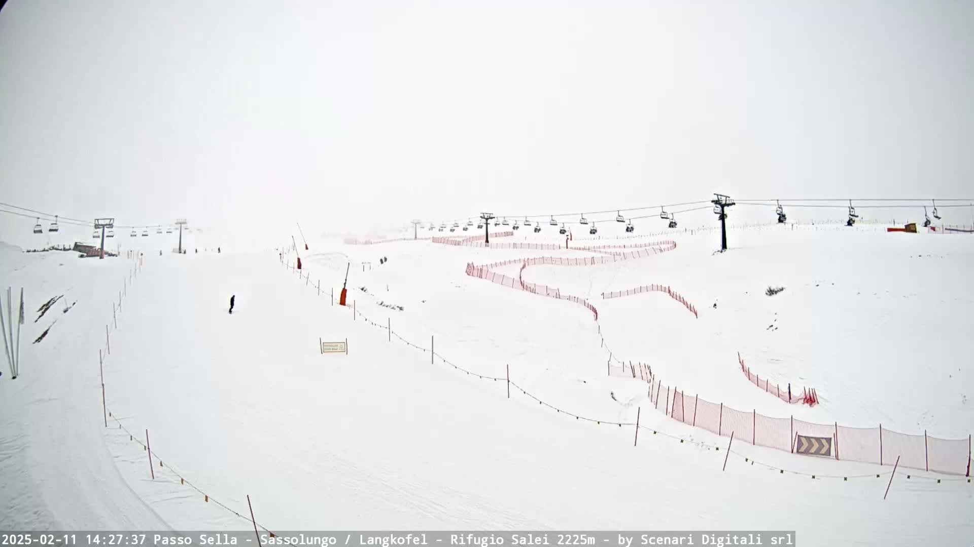 A snow-covered ski slope with chairlifts and safety netting is visible under foggy or overcast conditions.