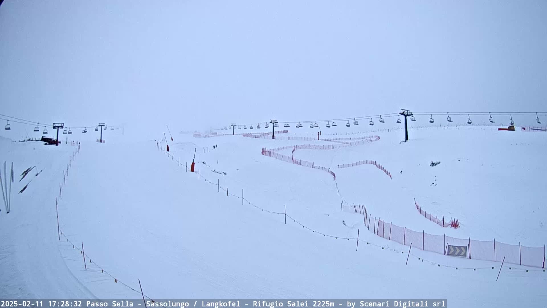 A snow-covered ski slope with chairlifts and red safety nets under a foggy sky.