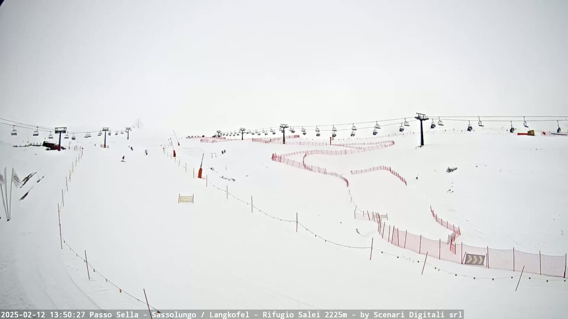 A snow-covered ski slope with several chairlifts and red safety nets is visible in overcast conditions.
