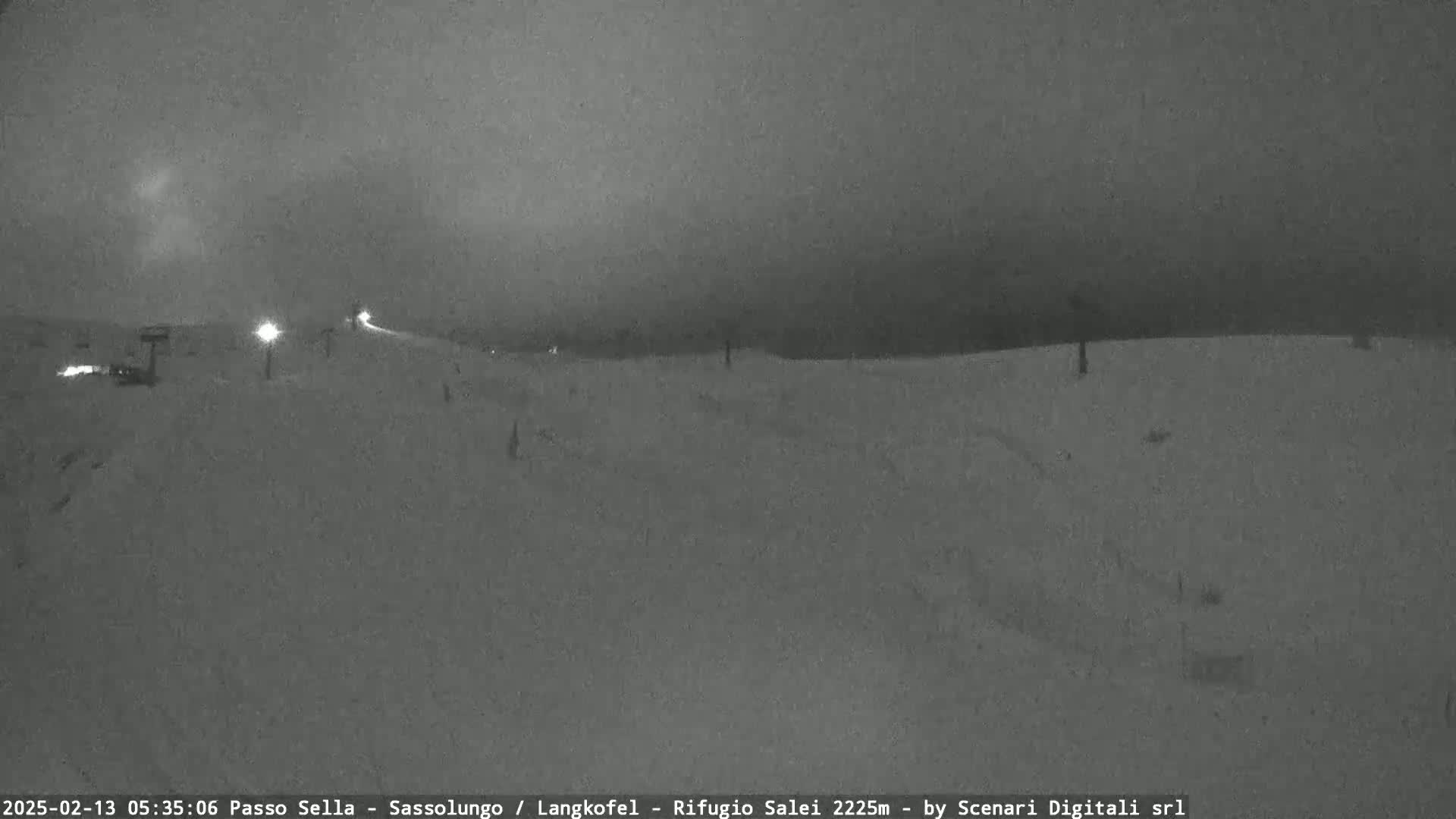 A snow-covered landscape is visible at night under a dark, cloudy sky, with a few lights illuminating the scene in the distance.
