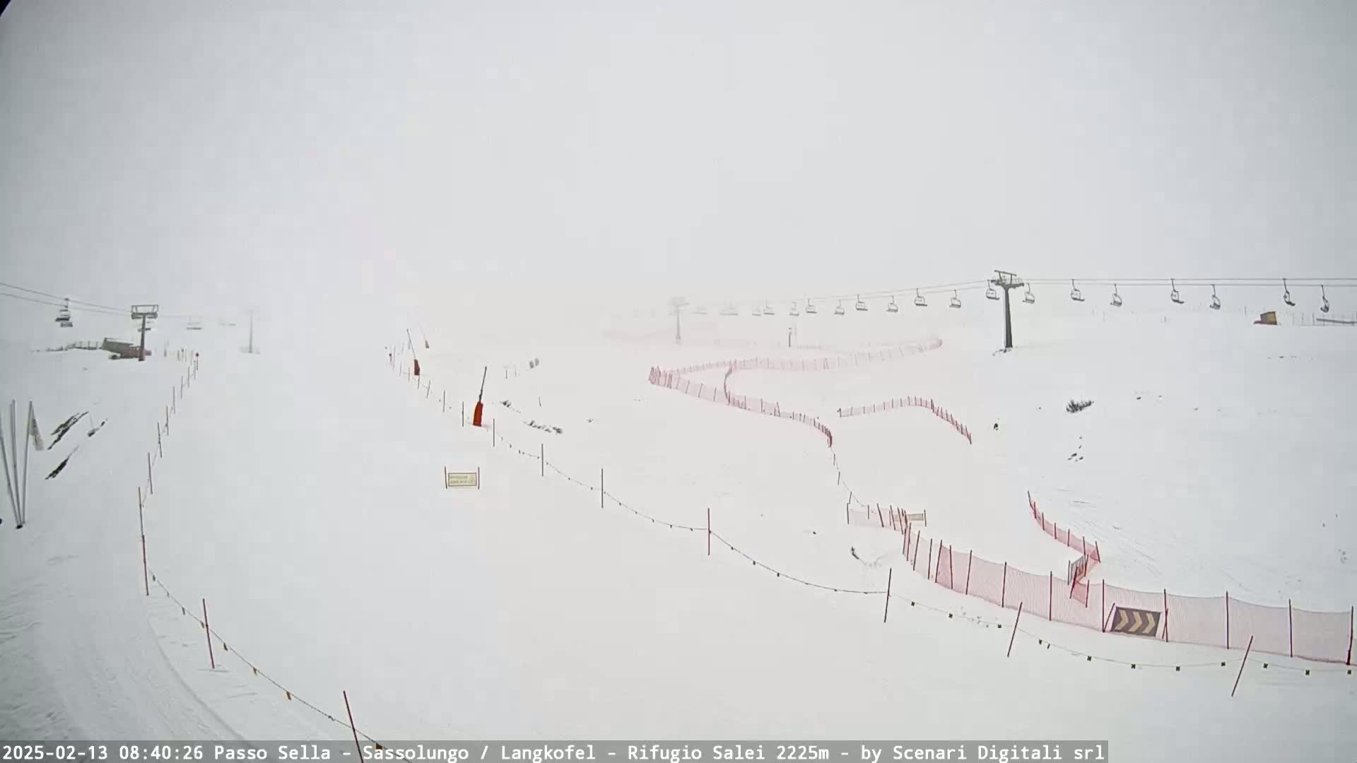 A snow-covered ski slope with chairlifts and red safety fences is visible in heavy fog or snow.