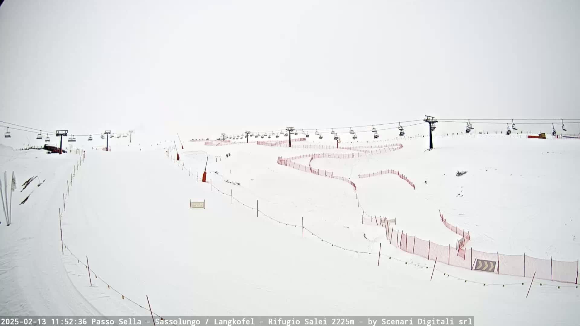 A snow-covered ski slope with chairlifts and red safety nets under an overcast sky.