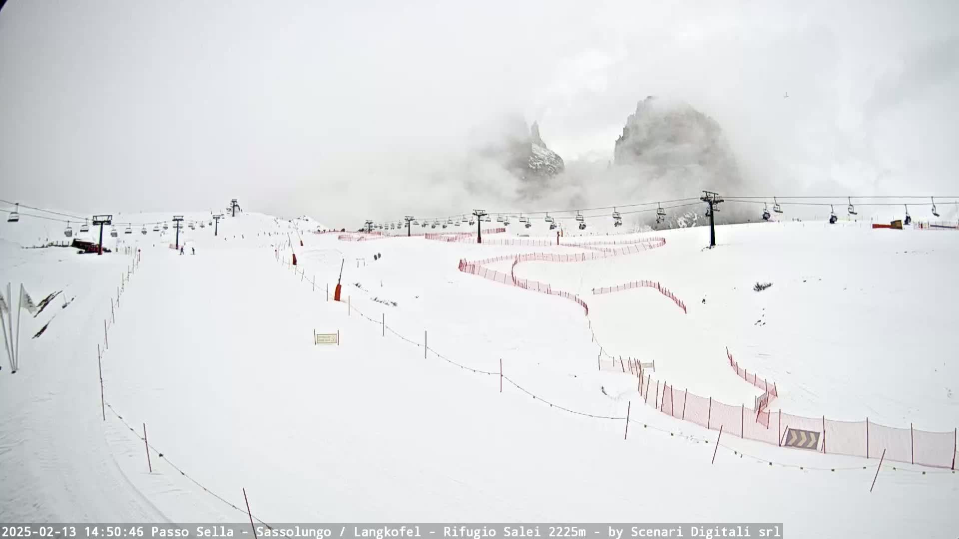 A snowy ski slope with several chairlifts and red safety nets, partially obscured by fog in the background.