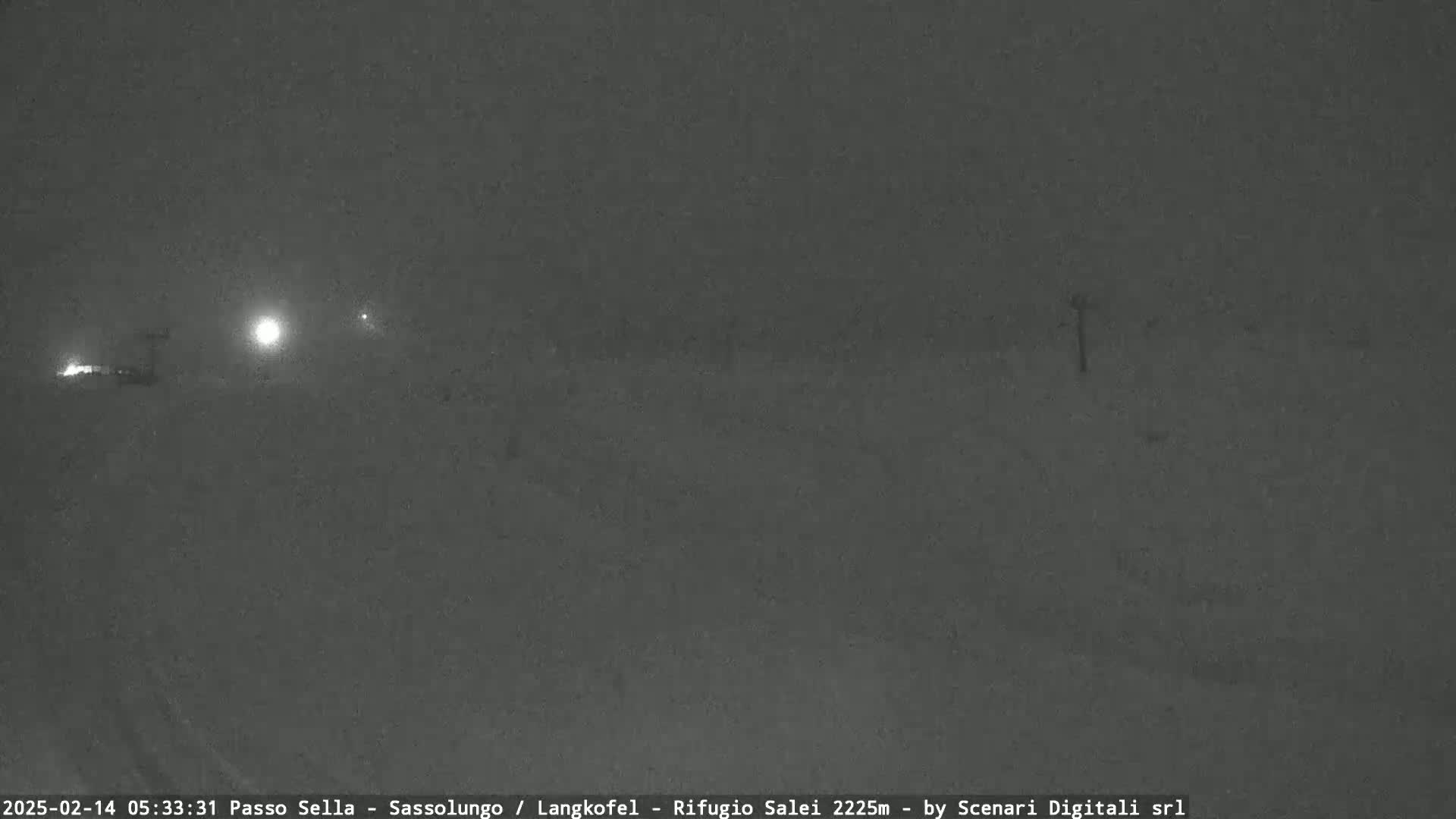 A snow-covered road is visible at night under heavy snowfall, with faint lights in the distance.