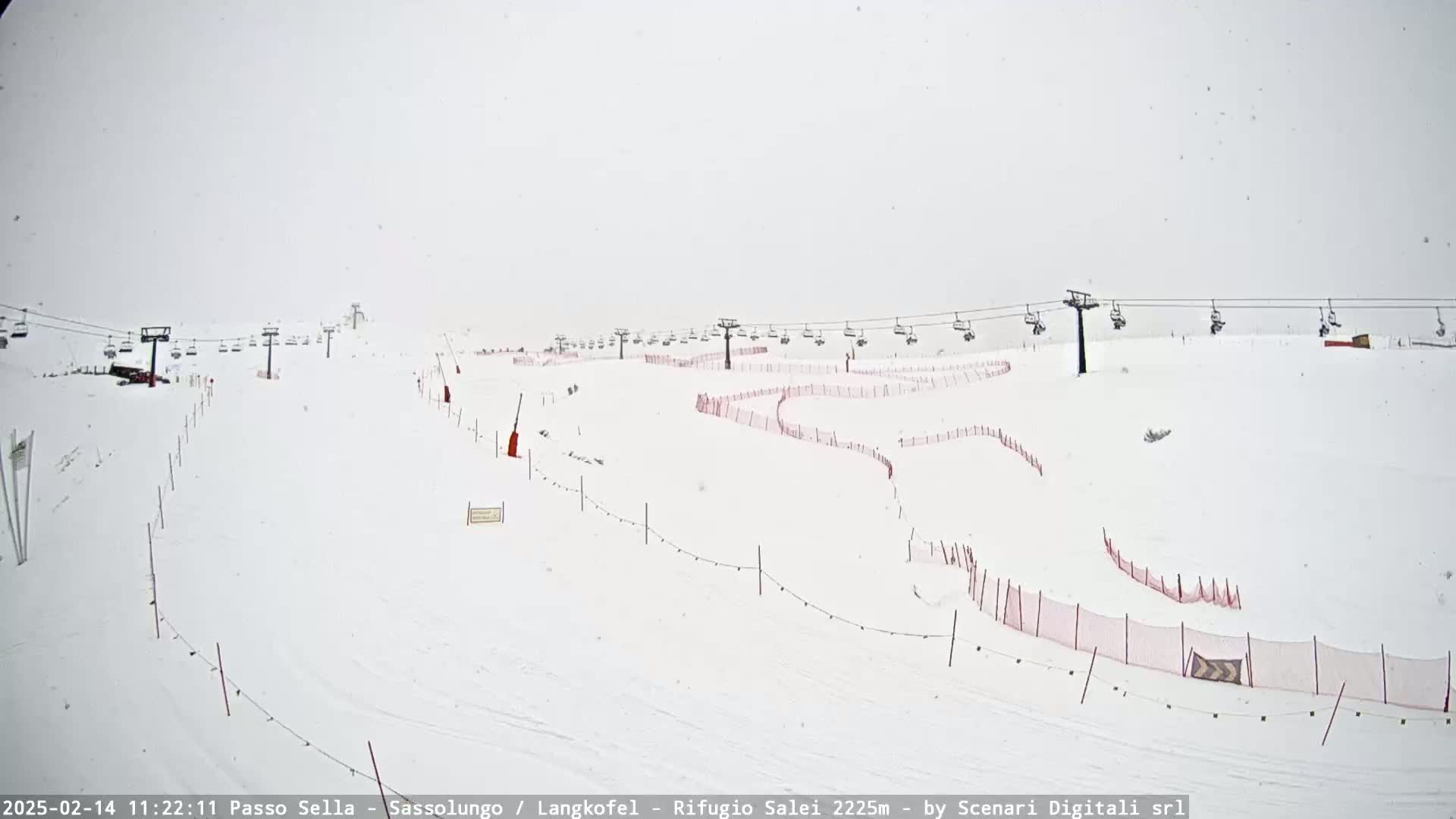 A snow-covered ski slope with chairlifts and red safety netting is visible during a light snowfall.
