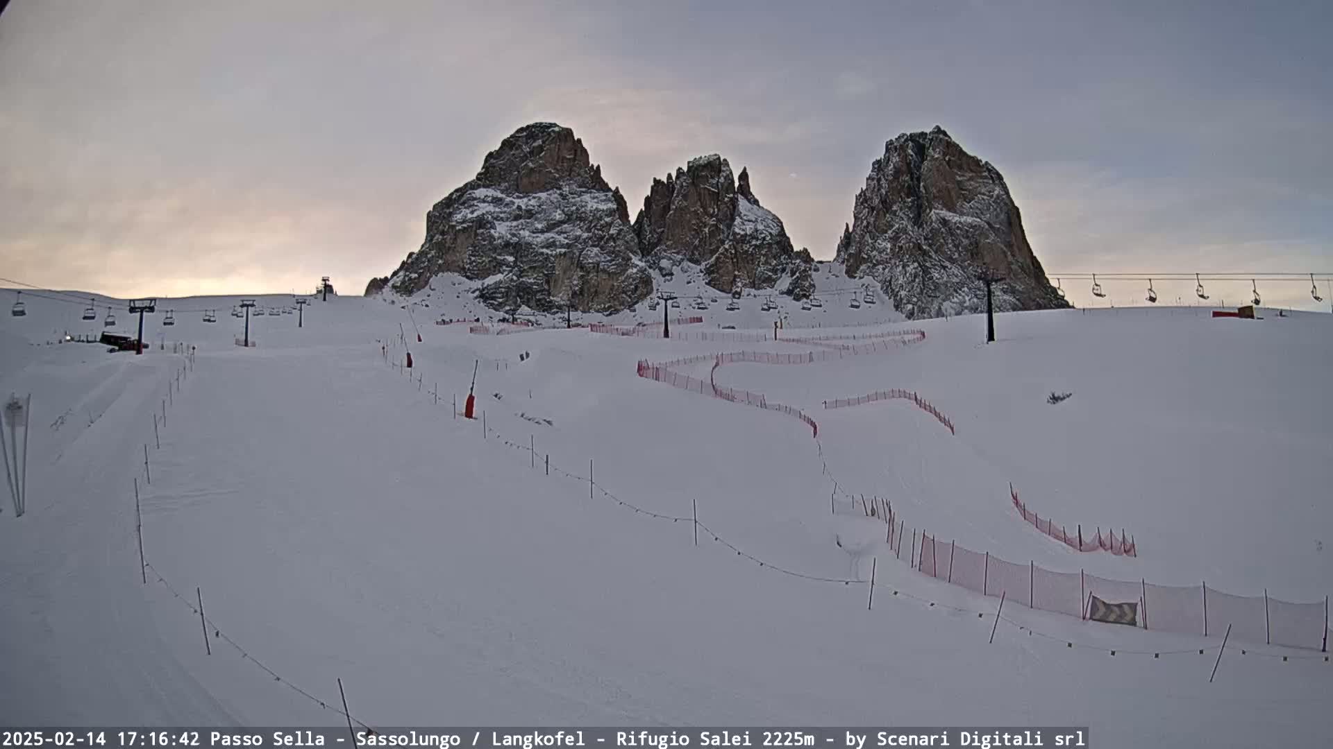 A snow-covered ski slope with chairlifts and snow-capped mountains in the background under a twilight sky.