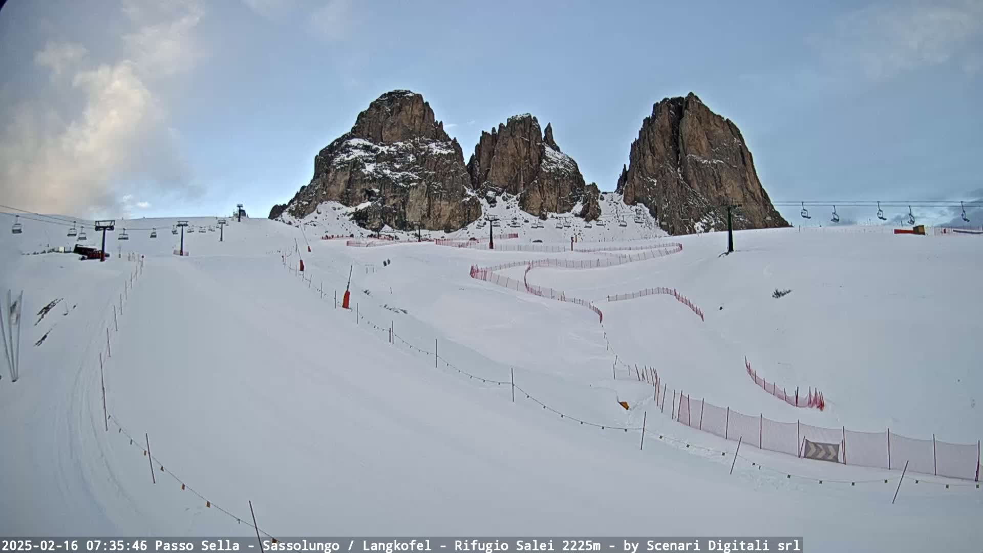 A snow-covered ski slope with several chairlifts and rocky mountain peaks in the background under a clear sky.