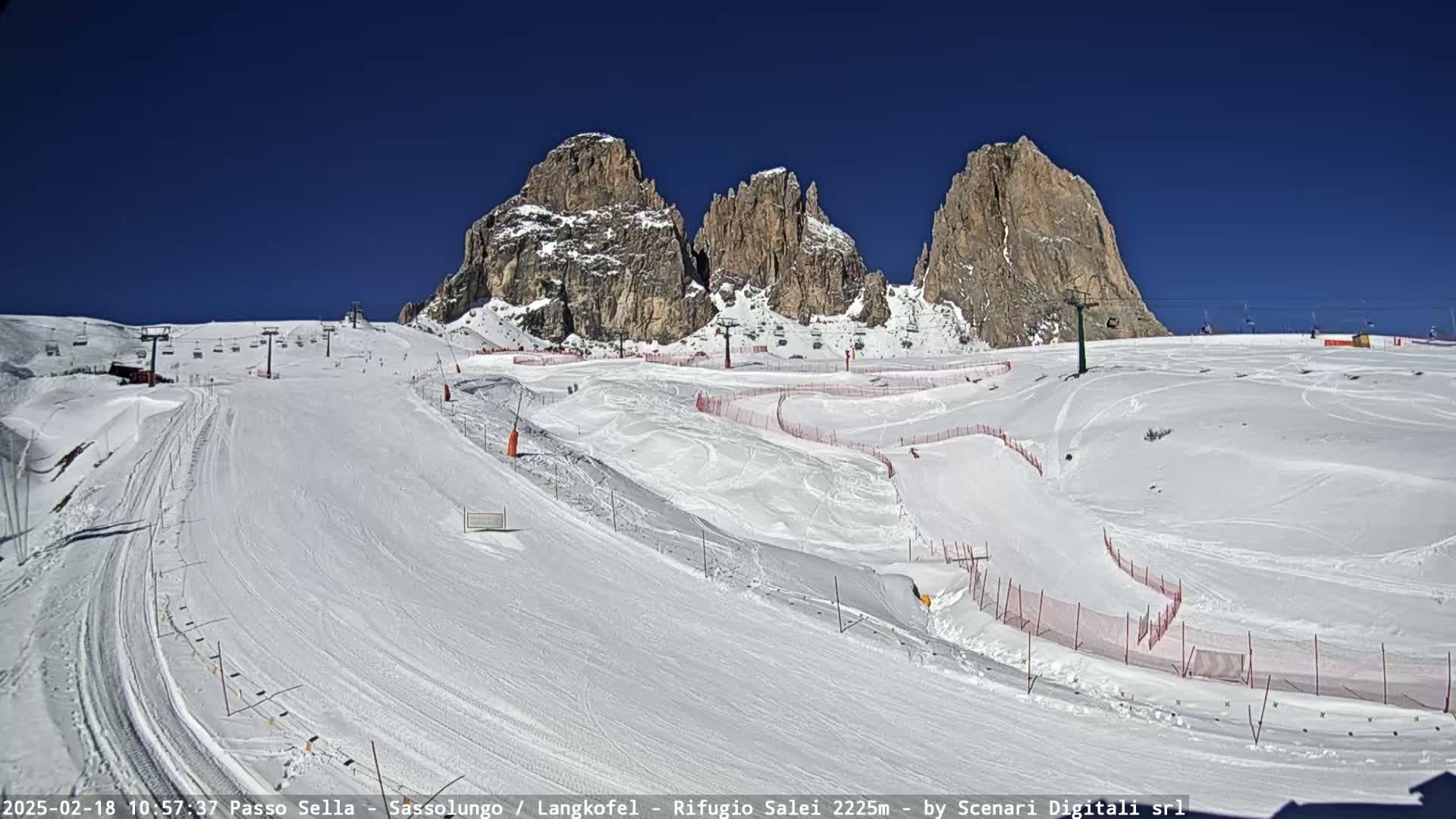 A snow-covered ski slope with ski lifts and mountain peaks in the background under a clear blue sky.