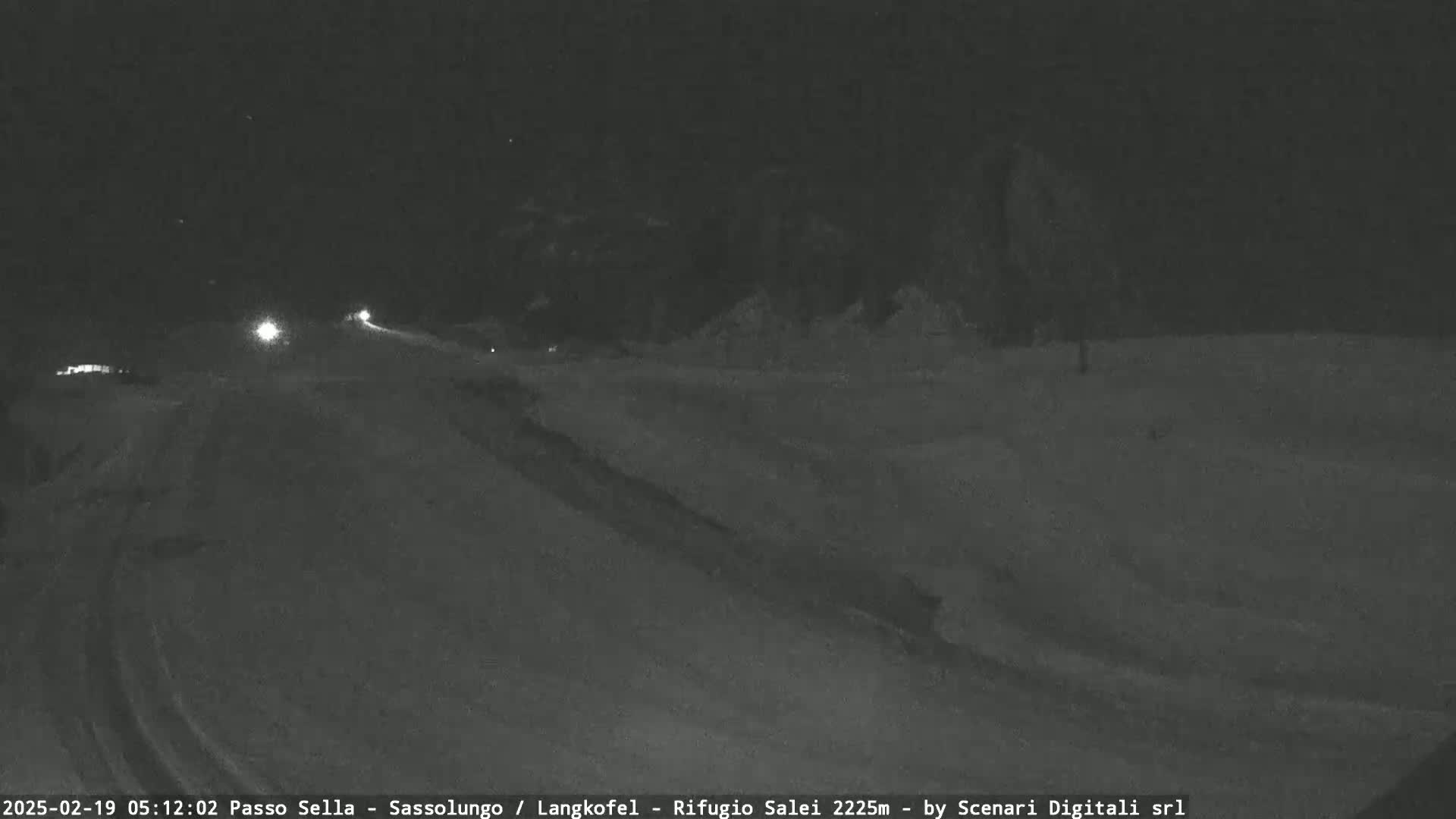 A snow-covered road at night with a few vehicle headlights visible in the distance.