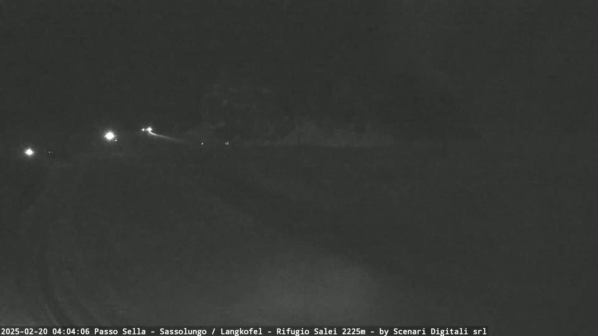At night, a dark road is visible with a few distant headlights and a dark, overcast sky.