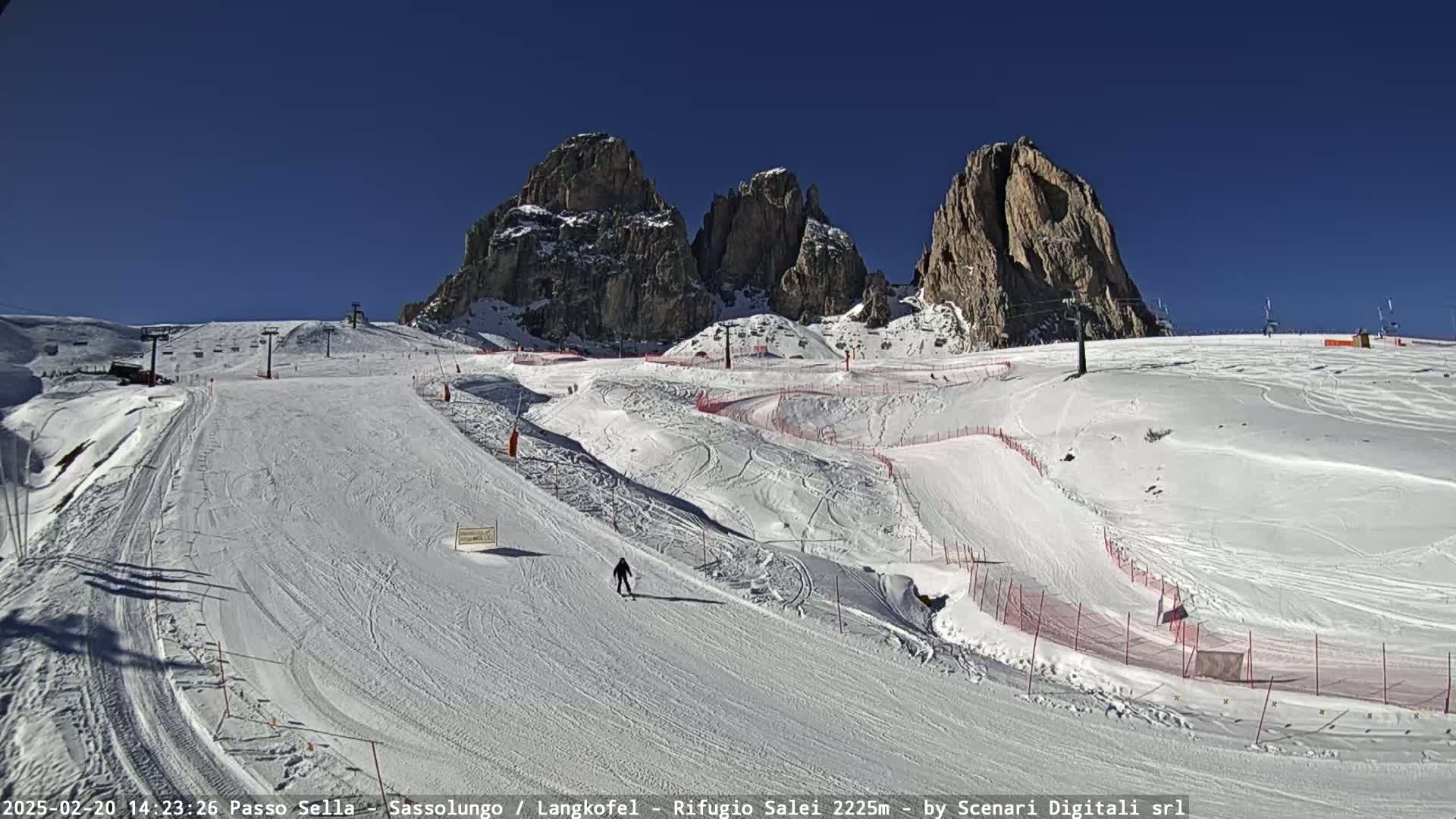 A snowy ski slope with a lone skier, surrounded by snow-covered mountains under a clear blue sky.