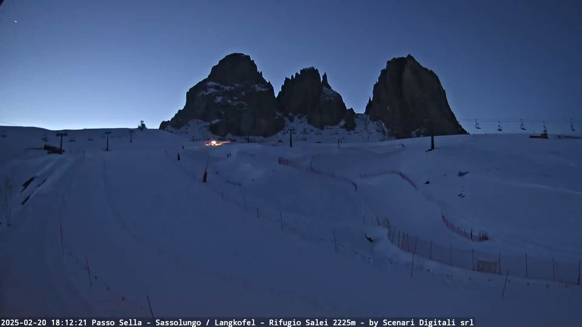 A snow-covered ski slope at twilight, with three prominent rock formations in the background and ski lifts visible.