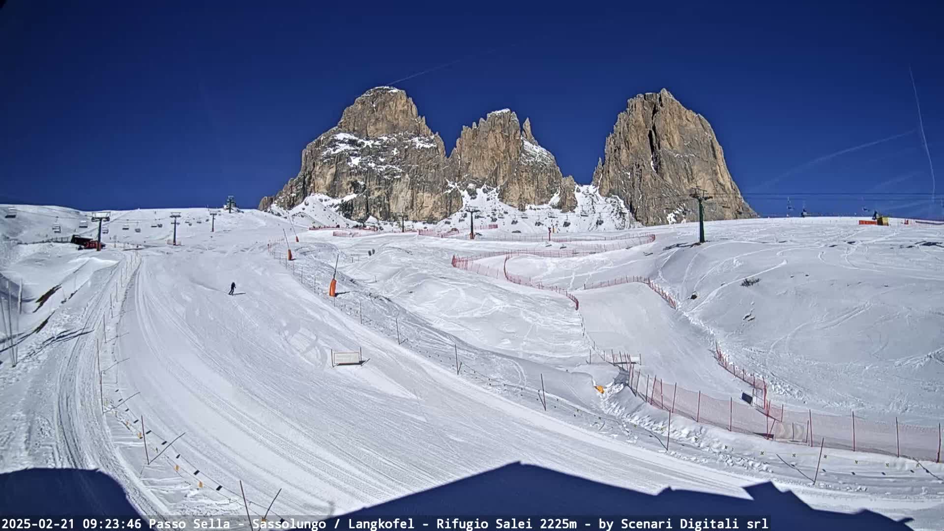 A sunny day at a snow-covered ski resort with several ski runs and lifts situated against a backdrop of towering, rocky mountains.