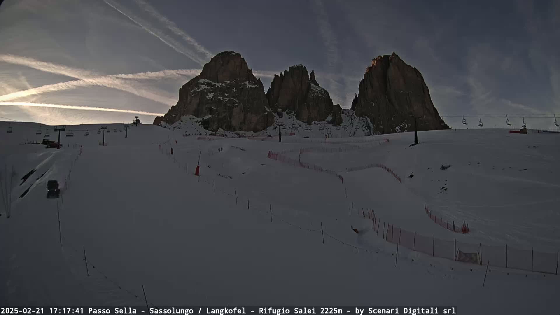 A snow-covered ski slope with several chairlifts and a mountain range in the background under a twilight sky.