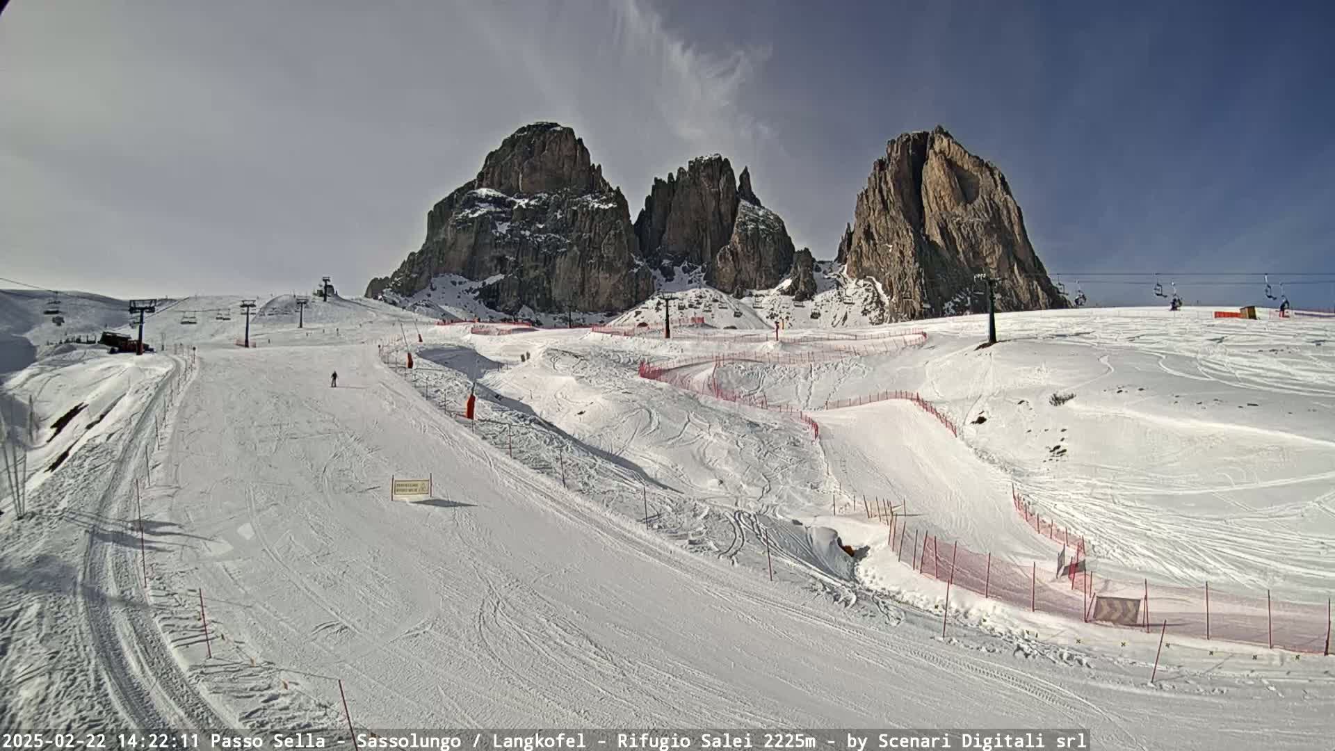 A snow-covered ski slope with several ski lifts and rocky mountain peaks in the background under a sunny sky.