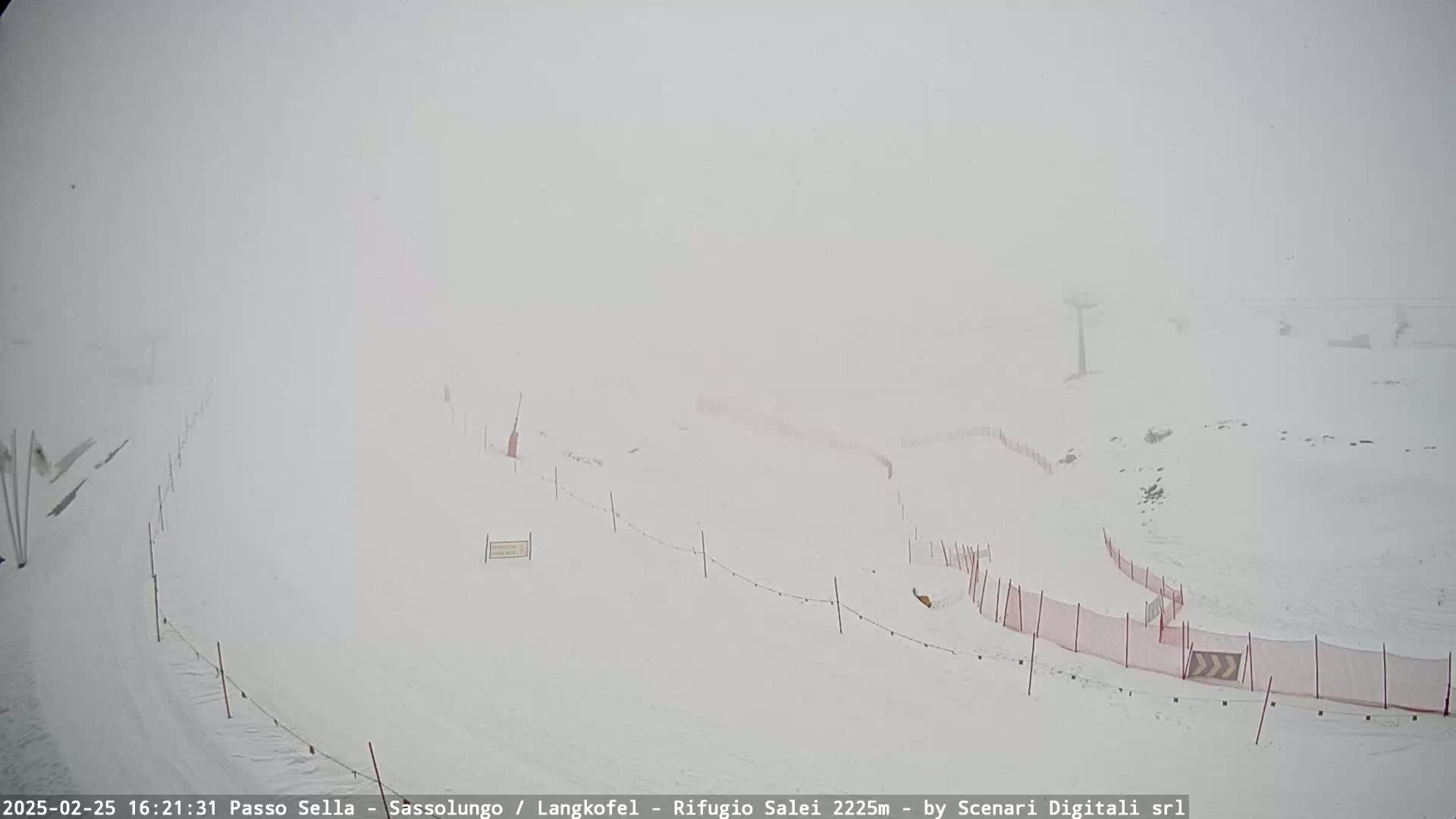 A snow-covered ski slope with sparse fencing is visible in heavy snow.