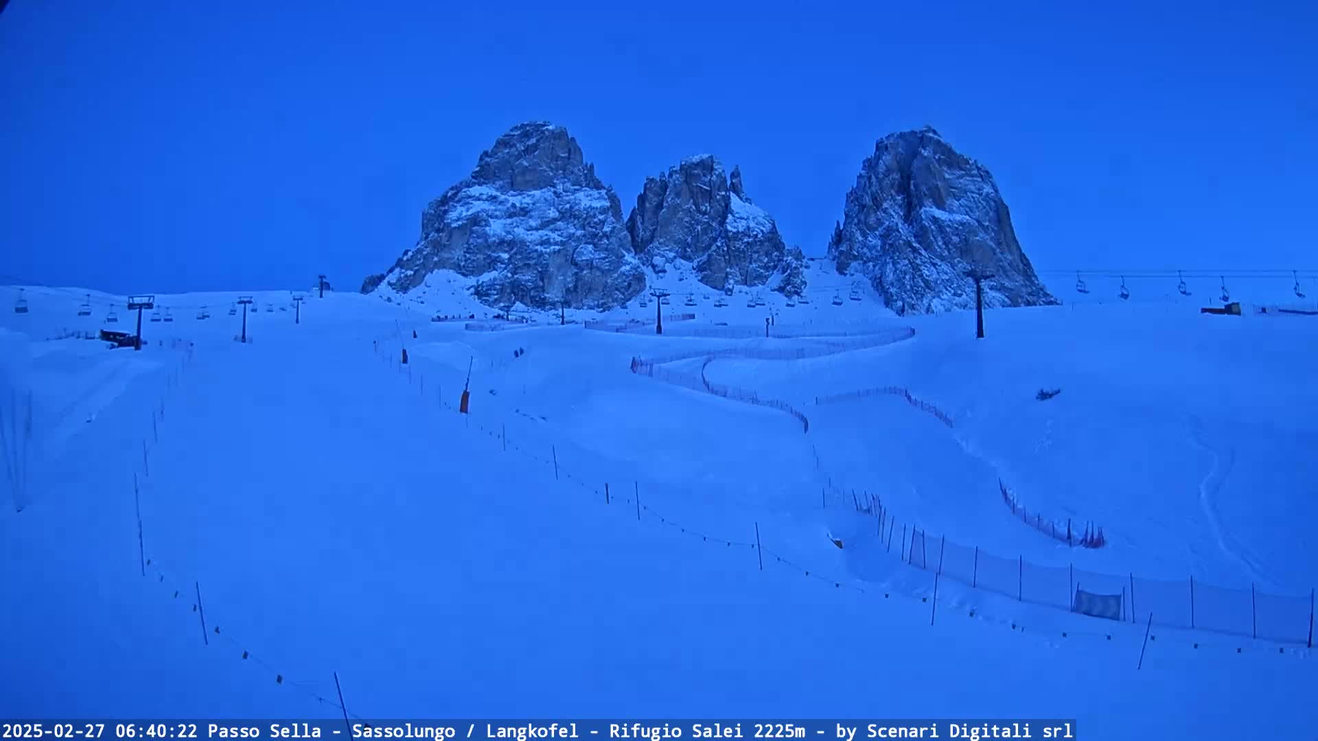 A snow-covered ski slope with chairlifts and snow-capped mountains in the background under a twilight sky.