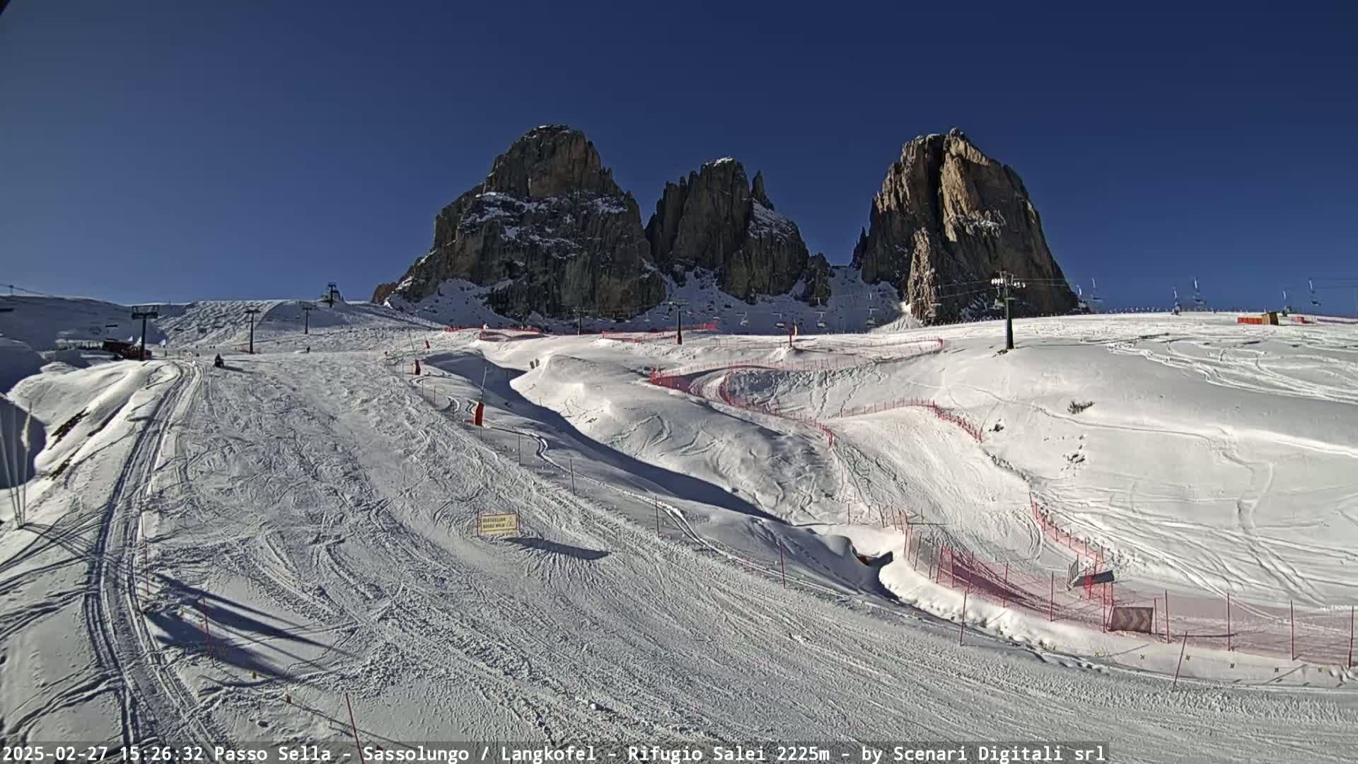 A snowy ski slope with ski lifts and several tall rock formations in the background under a clear blue sky.