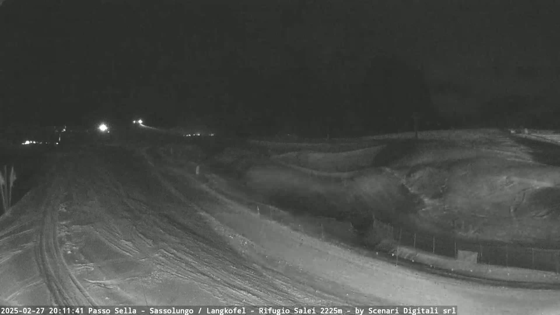 A nighttime, snow-covered landscape is visible, featuring a road with a few vehicles and gently sloping hills under a dark sky.